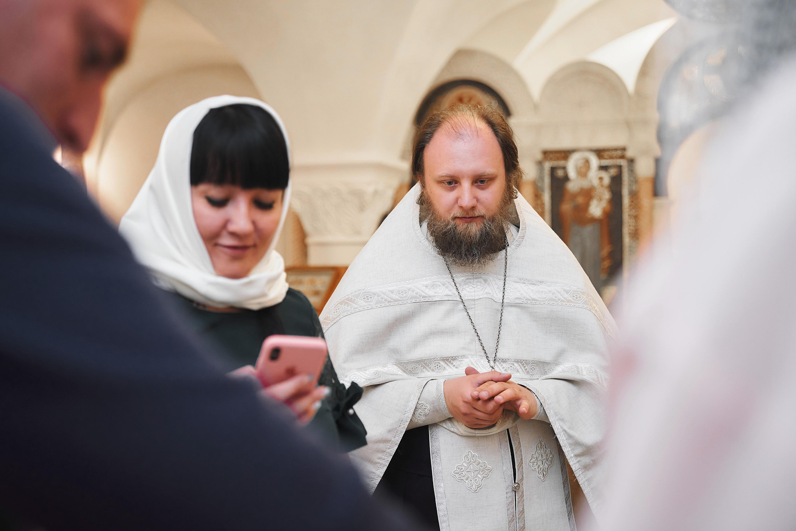 батюшка и гости смотрят на малыша во время крещения