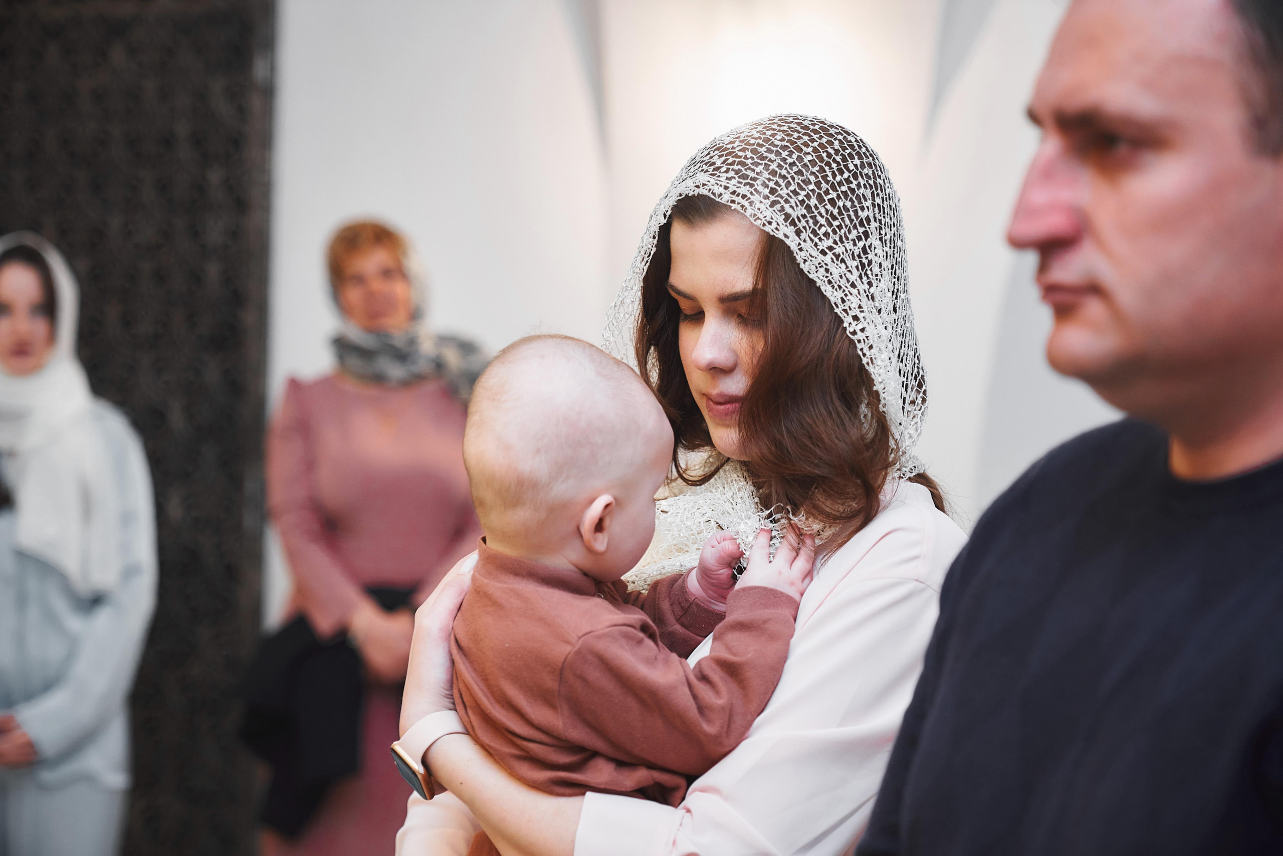 Крёстная Мама держит ребёнка на крещении в Храме Сергия Радонежского