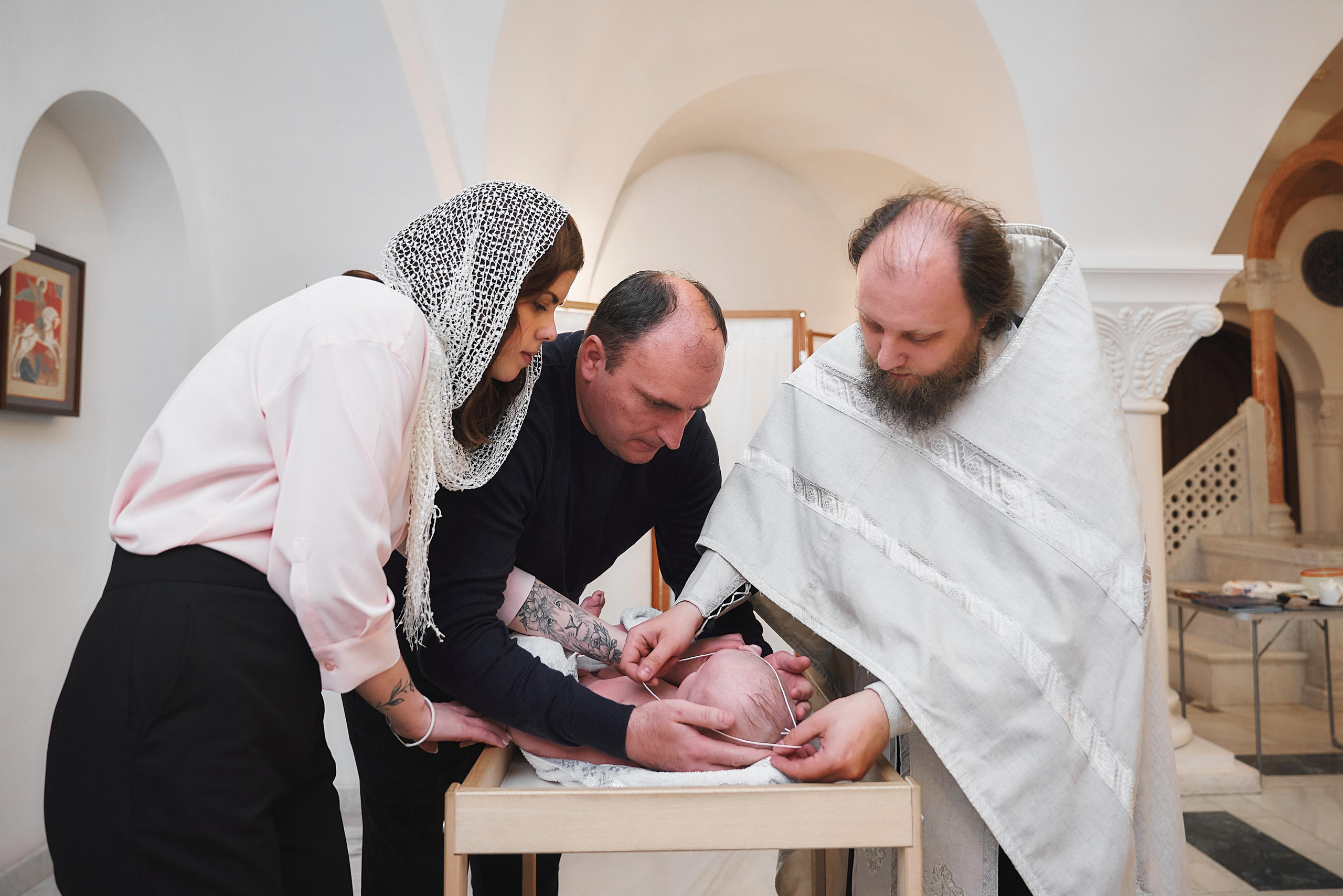 Батюшка и крёстные родители одевают нательный крестик на ребёнка в церкви Сергия Радонежского в Солнцево