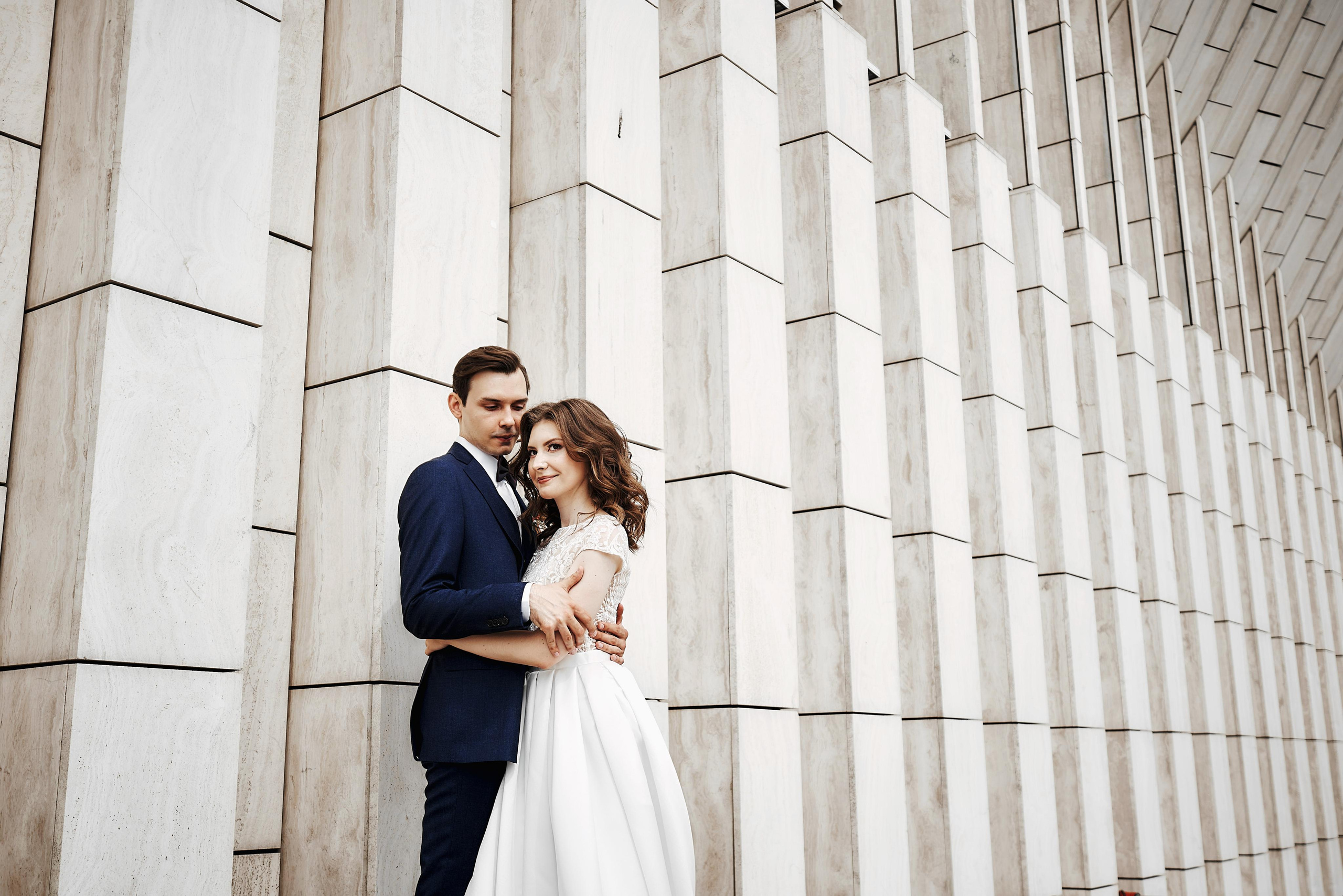 жених и невеста обнимаются у стены в парке Зарядье