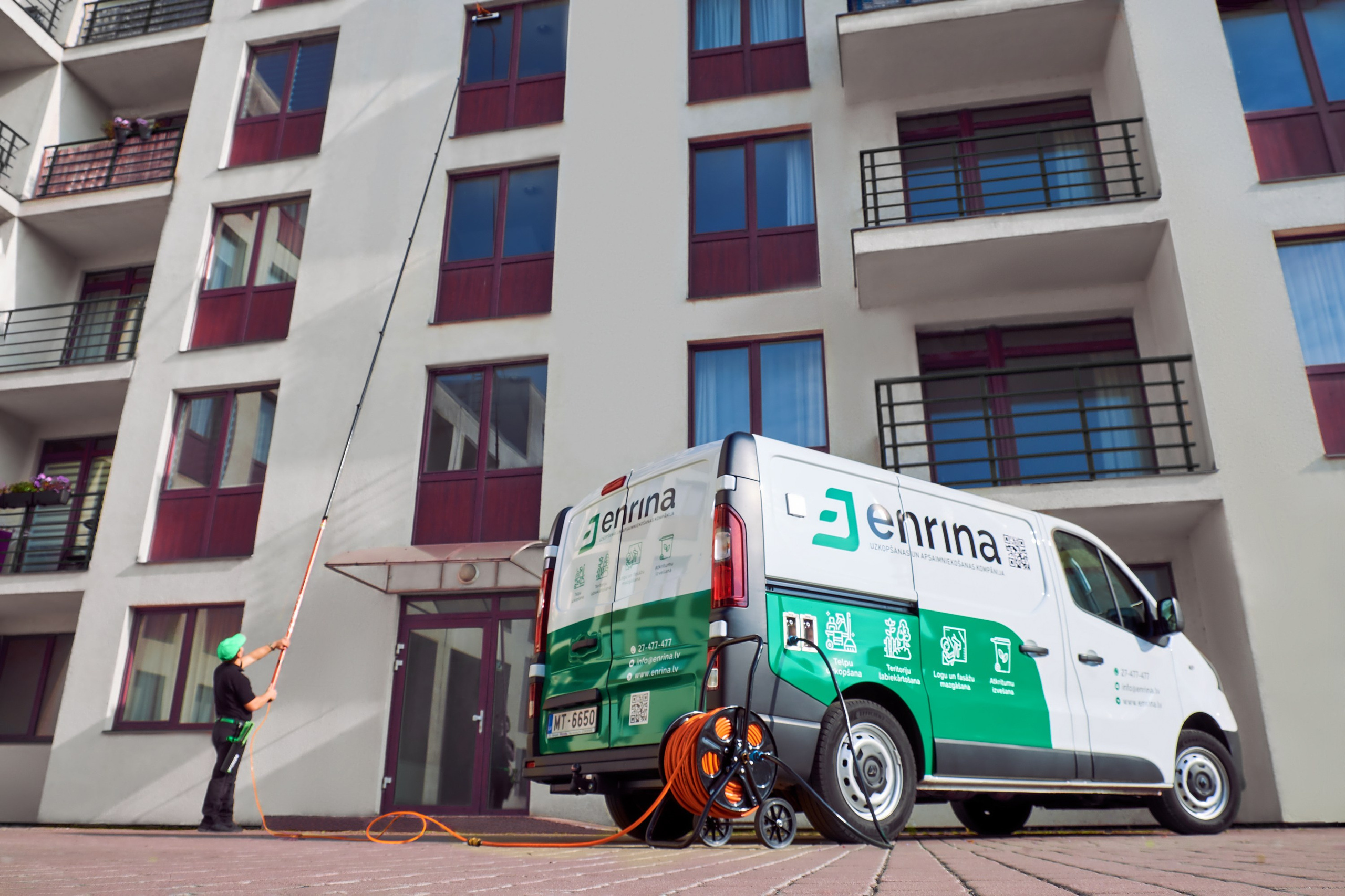 Коммерческая фотосъёмка работы клининговой компании: сотрудник выполняет высотную мойку фасада жилого комплекса, брендированный автомобиль компании на переднем плане.