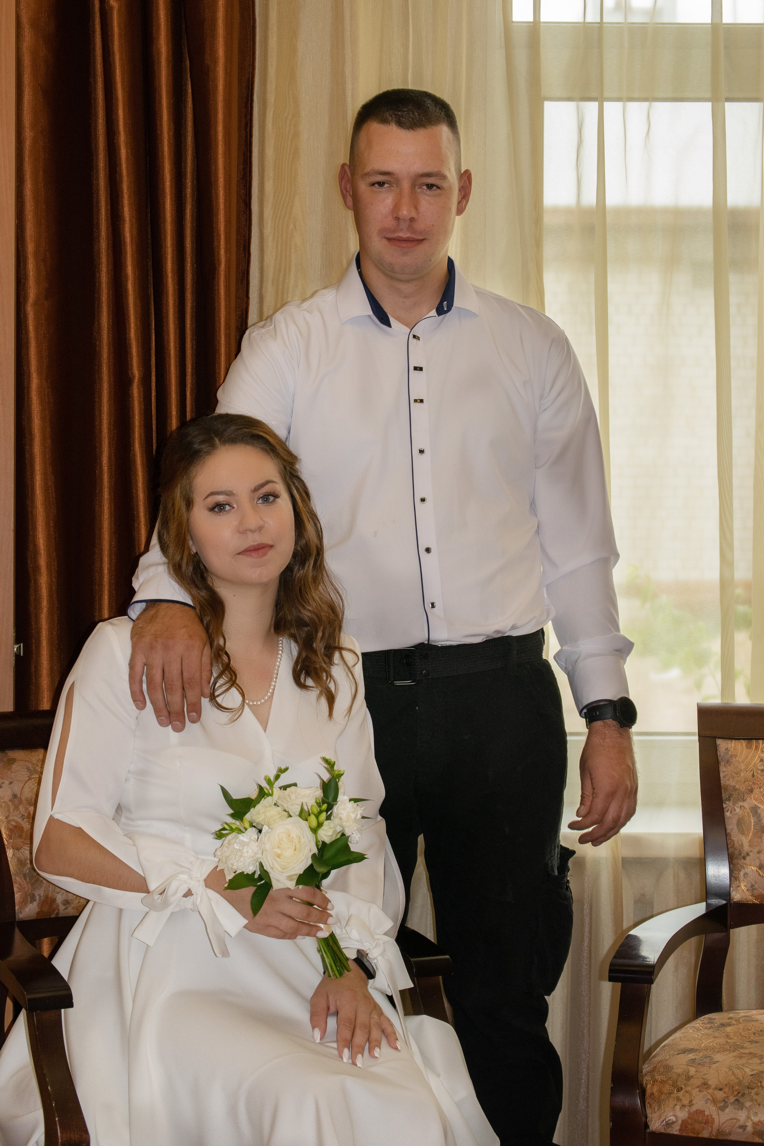 Фотосъемка молодоженов в Сортавальском Загсе Карелия. Невеста сидит, жених стоит рядом.
