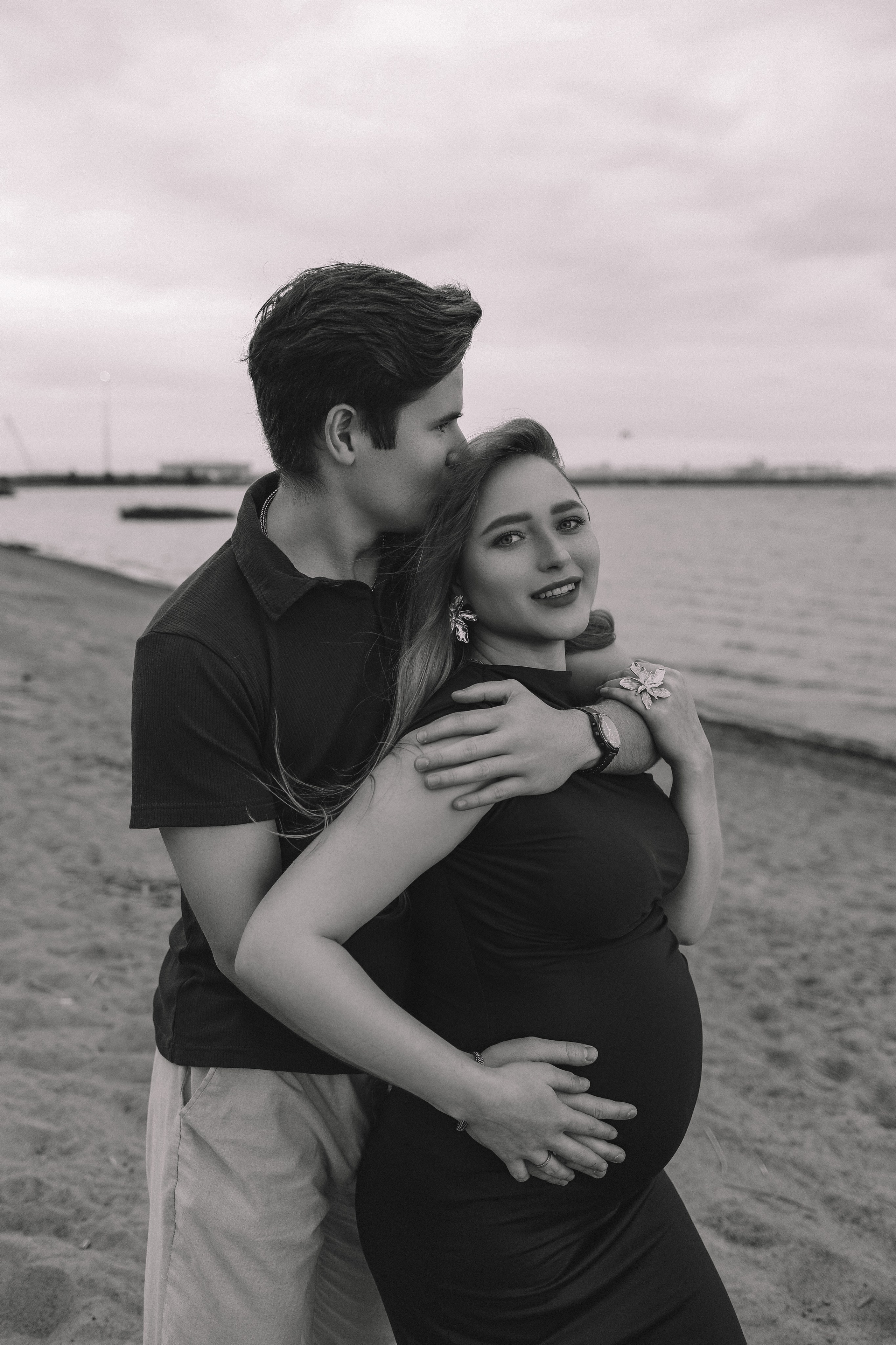 Пара обнимается, мужчина держит живот, черно-белое фото беременности