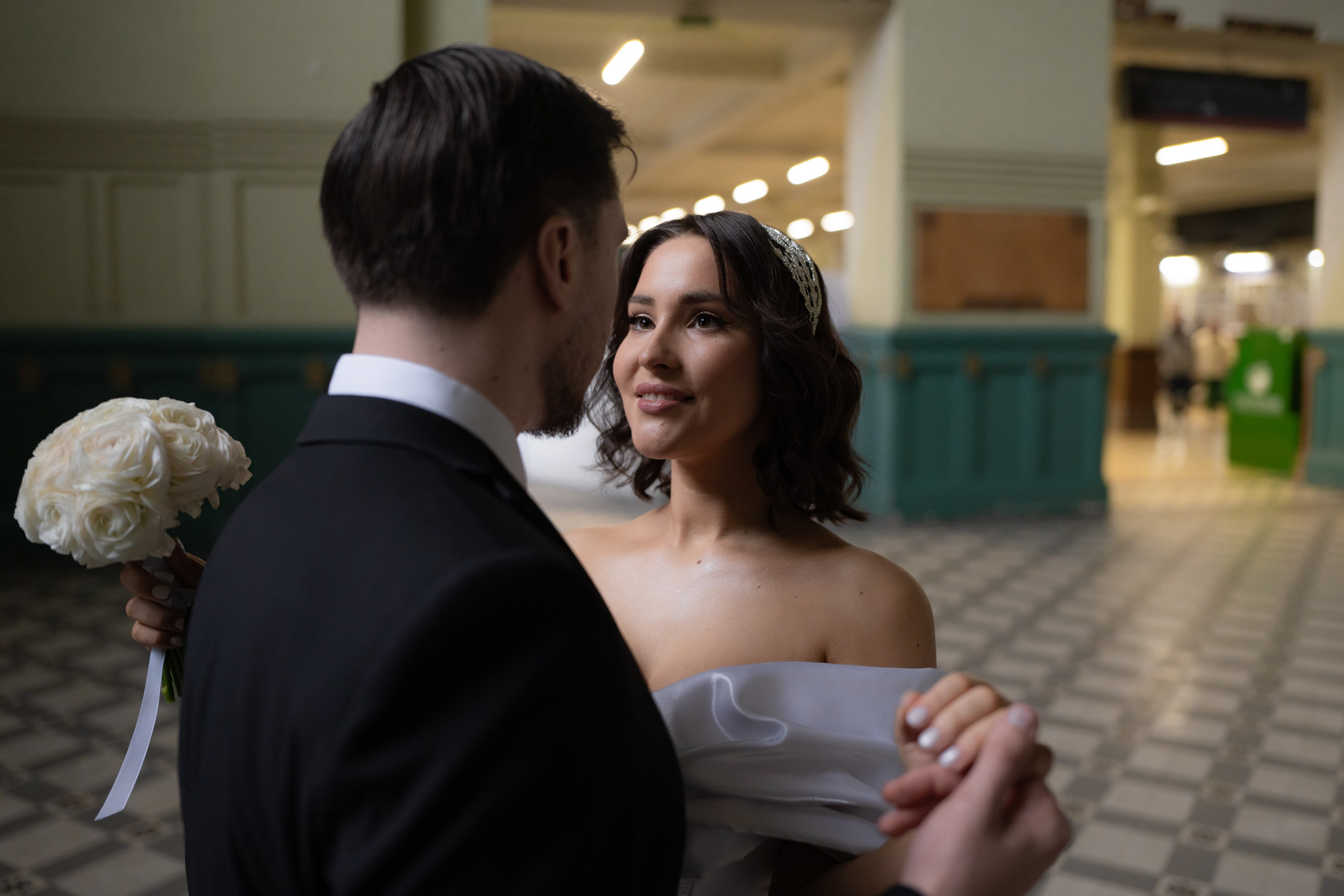 Жених с невестой танцуют и смотрят друг другу в глаза в зале Витебского вокзала на свадебной фотосессии в Санкт-Петербурге