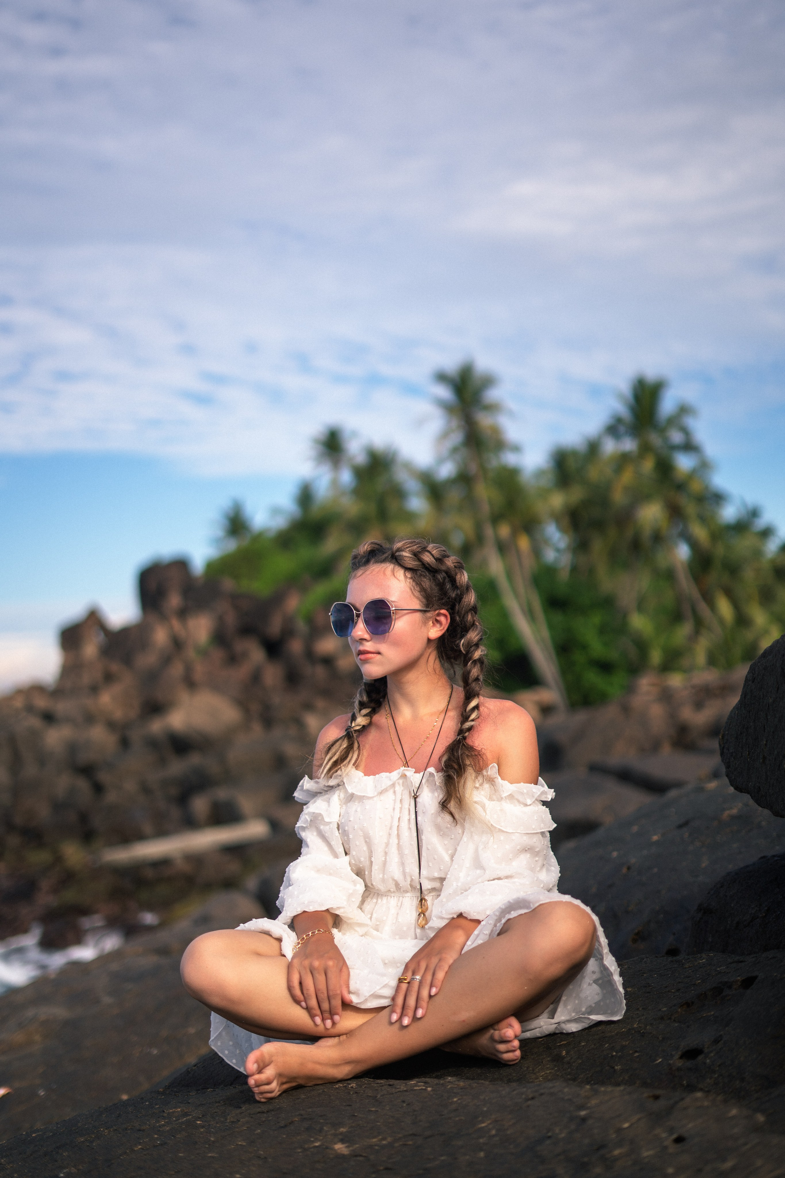 a young beauty in a white dress and glasses with a smiling face on the rocks