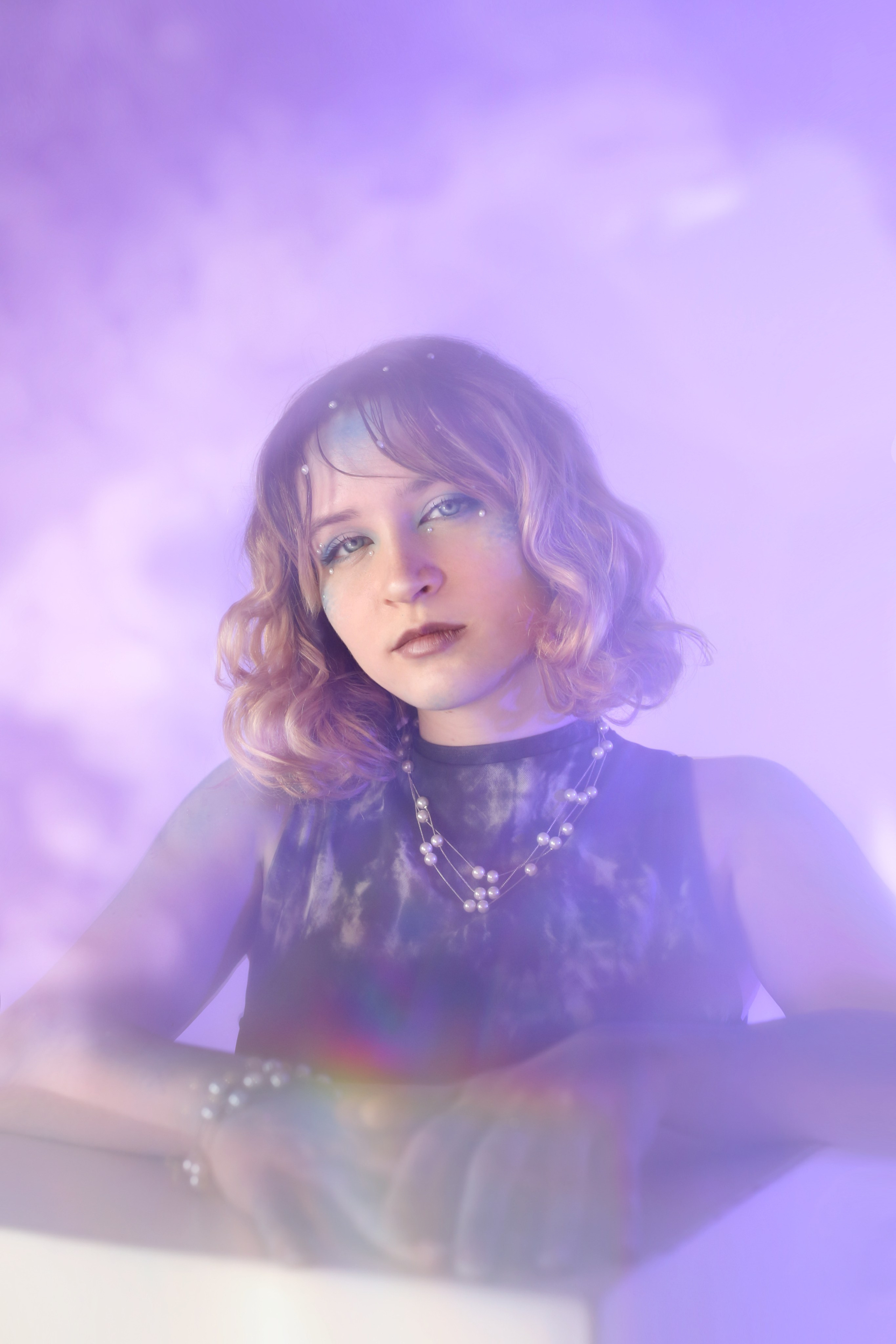 Мистический портрет: девушка в черном платье смотрит в камеру на фоне фиолетового света