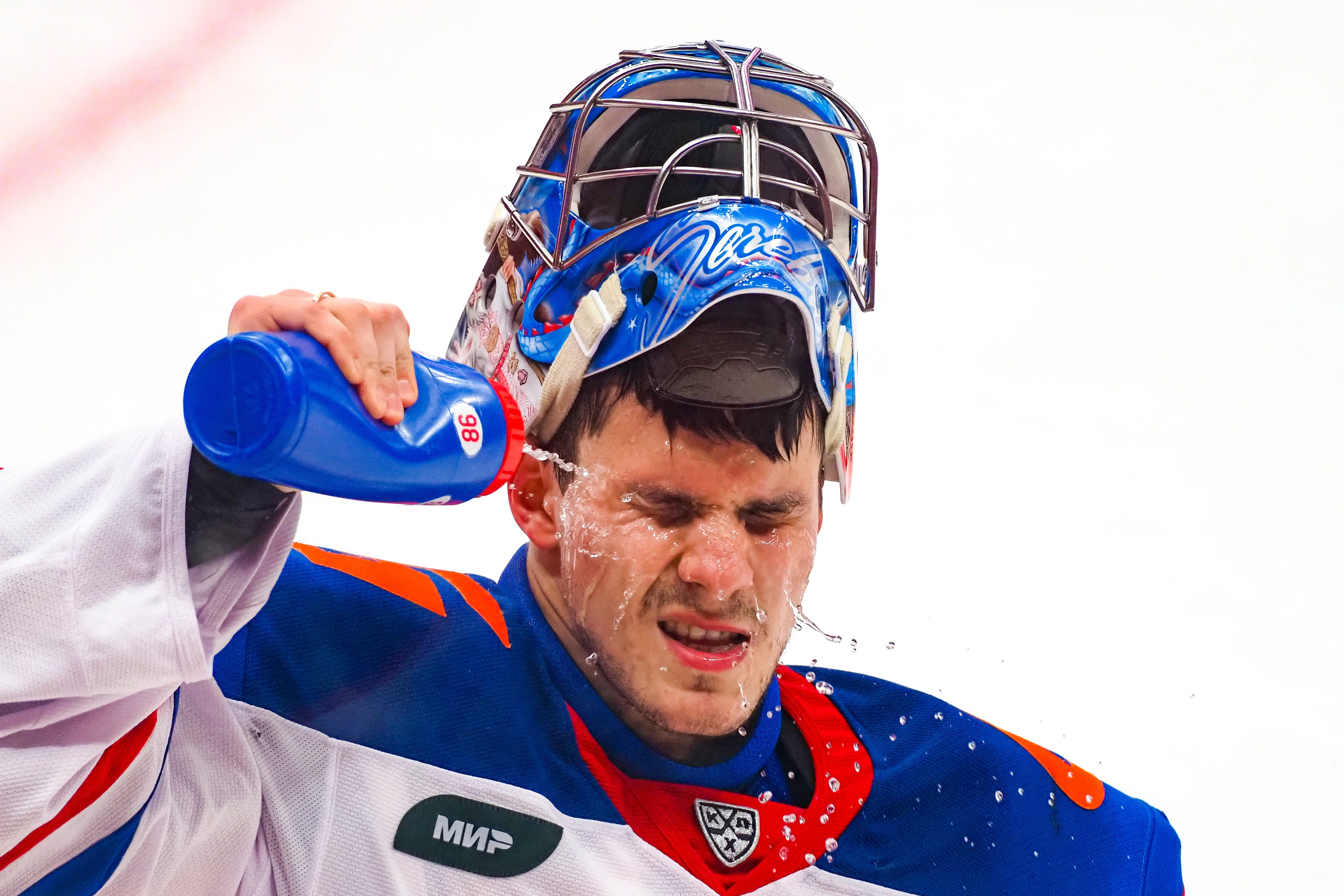 Хоккейный вратарь пьет воду в перерыве и брызгает ее себе на лицо