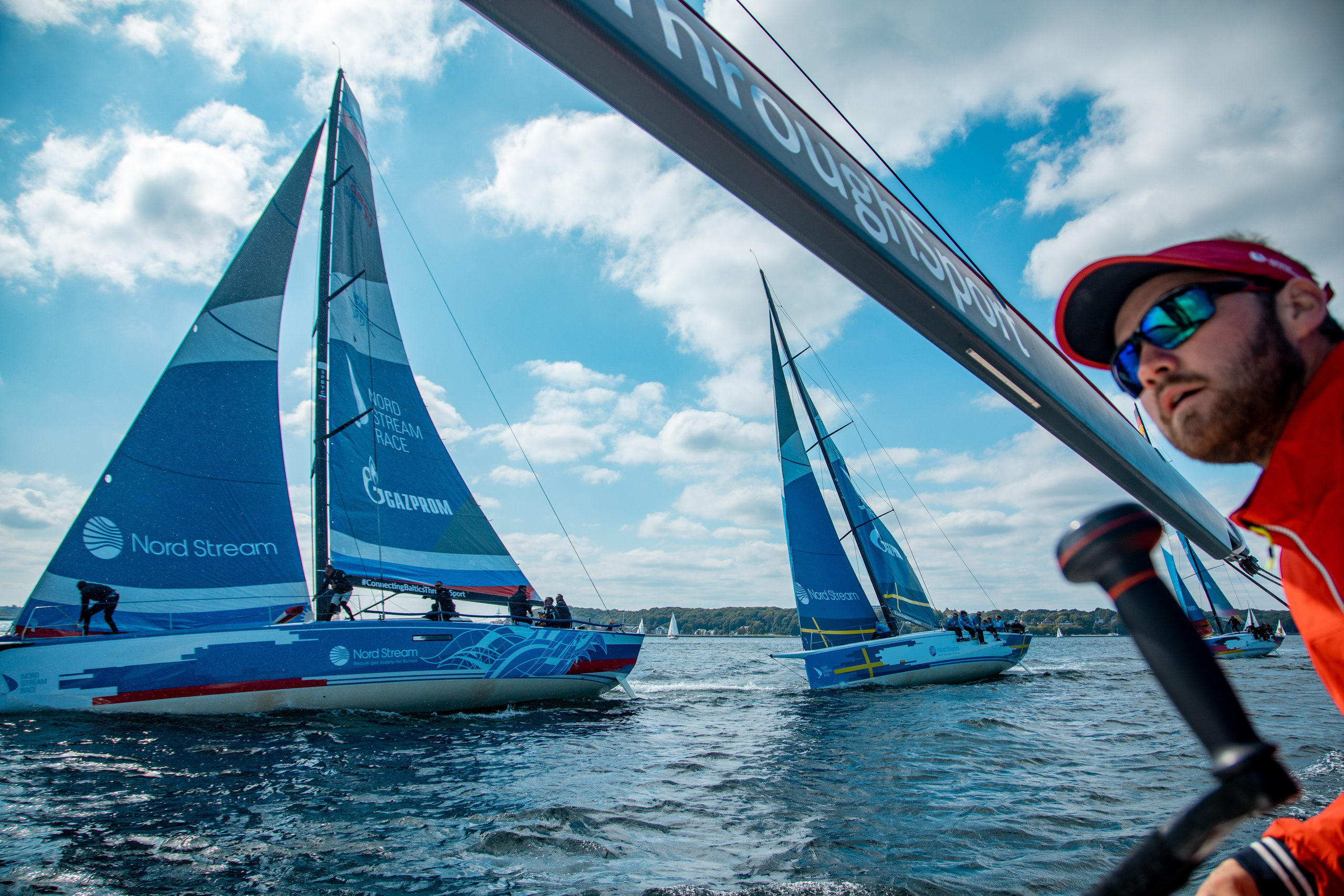 Яхтсмен в очках и кепке на фоне гика на парусной регате на Балтийском море.