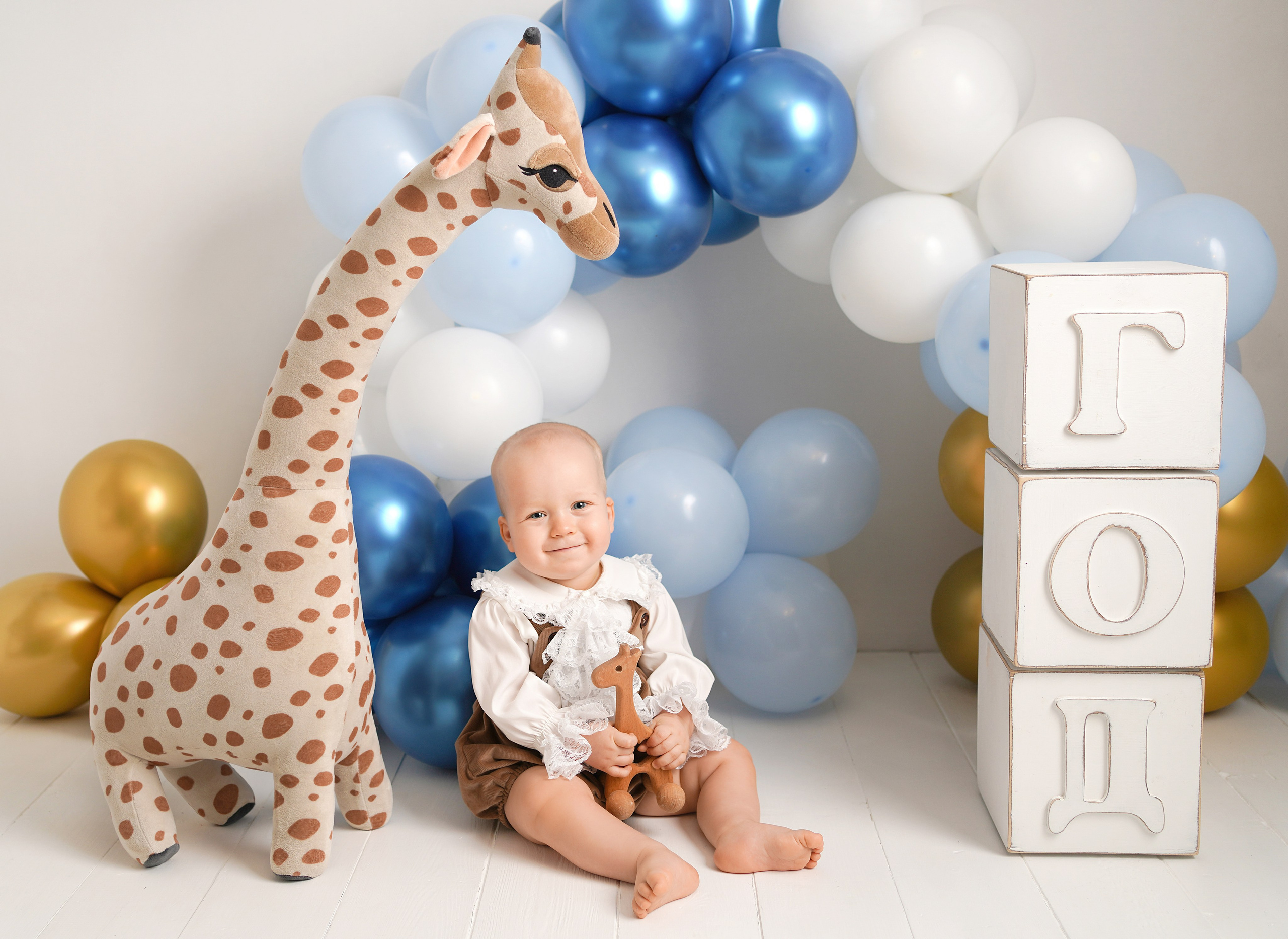 Малыш сфотографирован с жирафом и большими кубиками Год.