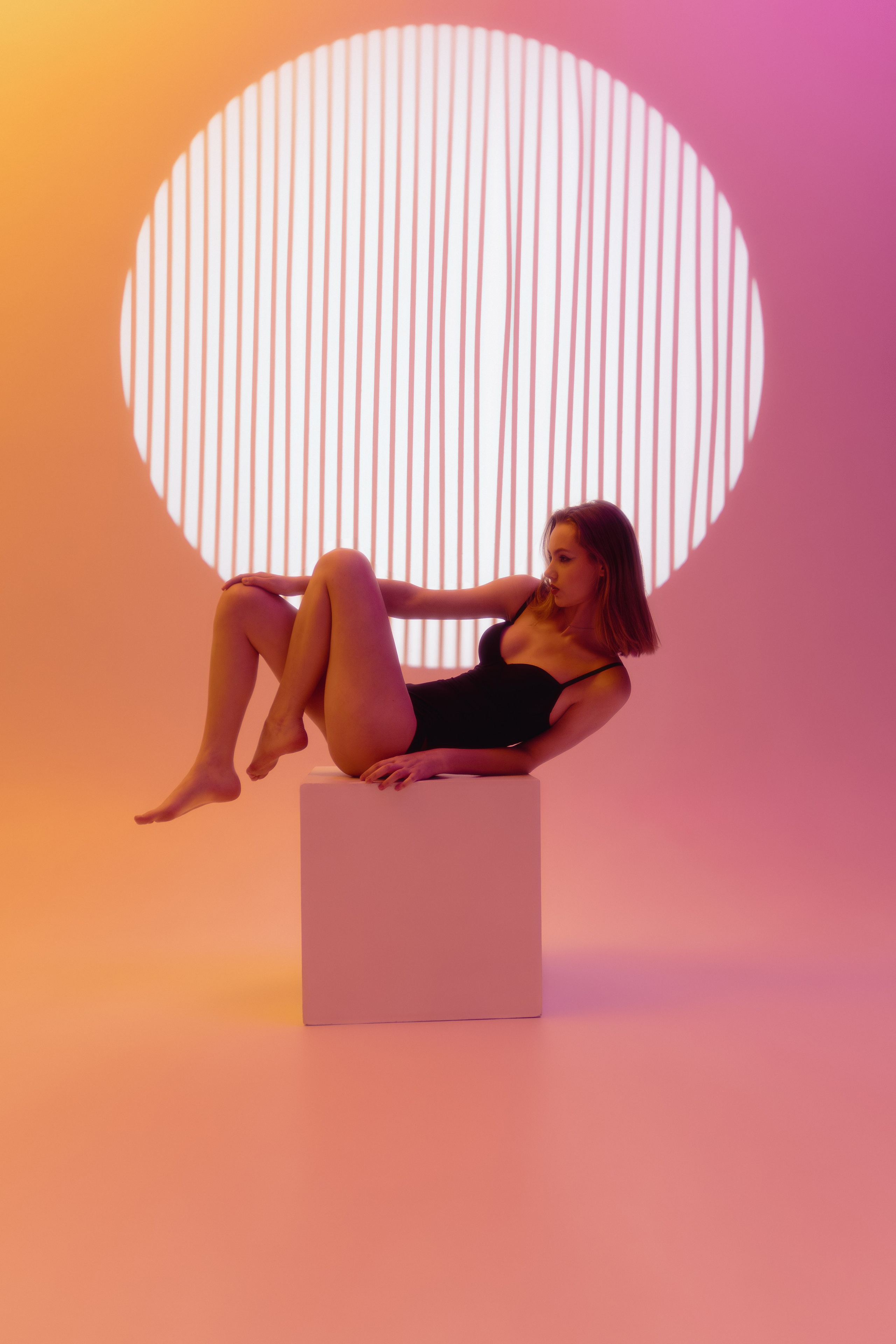 Девушка в боди позирует на белом кубе в фотостудии 