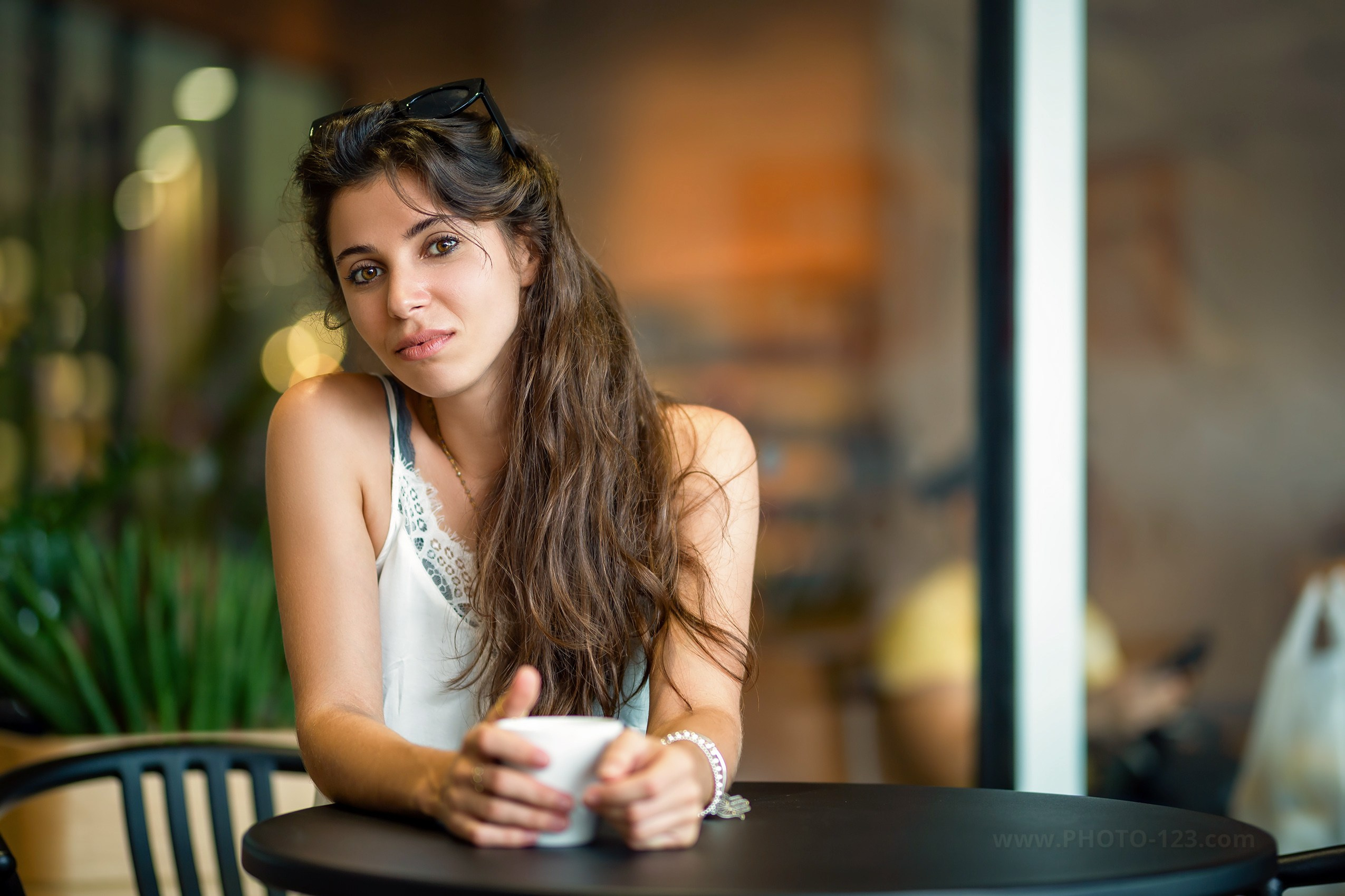 Portrait of a young woman sitting in a cafe, holding a coffee cup, photographed in soft natural light with shallow depth of field. Fashion and beauty portrait with warm tones, expressive eyes and relaxed mood. Professional lifestyle and beauty photography by a commercial photographer in Phu Quoc, Vietnam, focused on personal branding, fashion campaigns, and editorial shoots