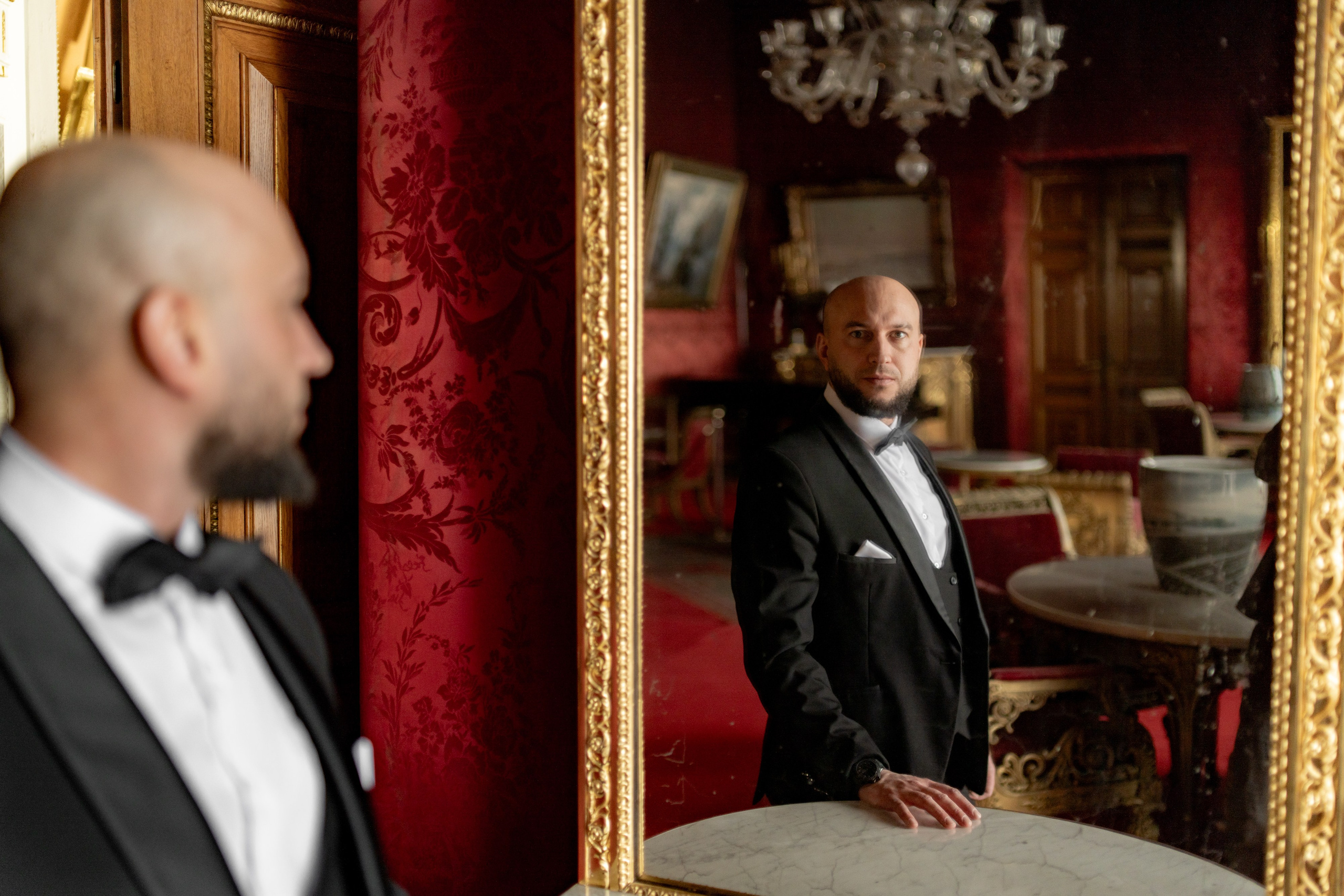 Жених красиво смотрит на себя в зеркало во Дворце Великого Князя Владимира в красном зале