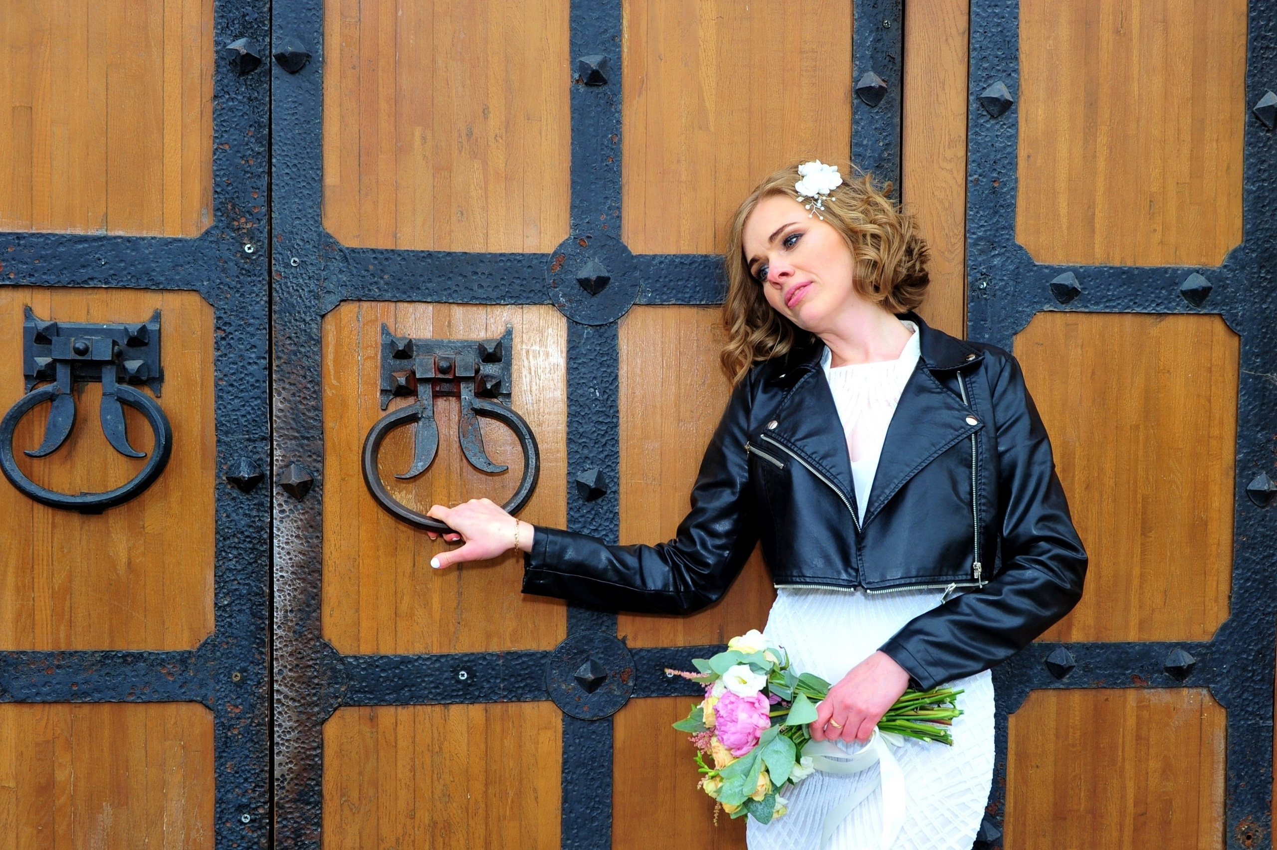 Свадьба в Царицыно хмурым прохладным летним днём, невеста задумчиво стоит у старинных деревянных дверей и держится за кованную дверную ручку