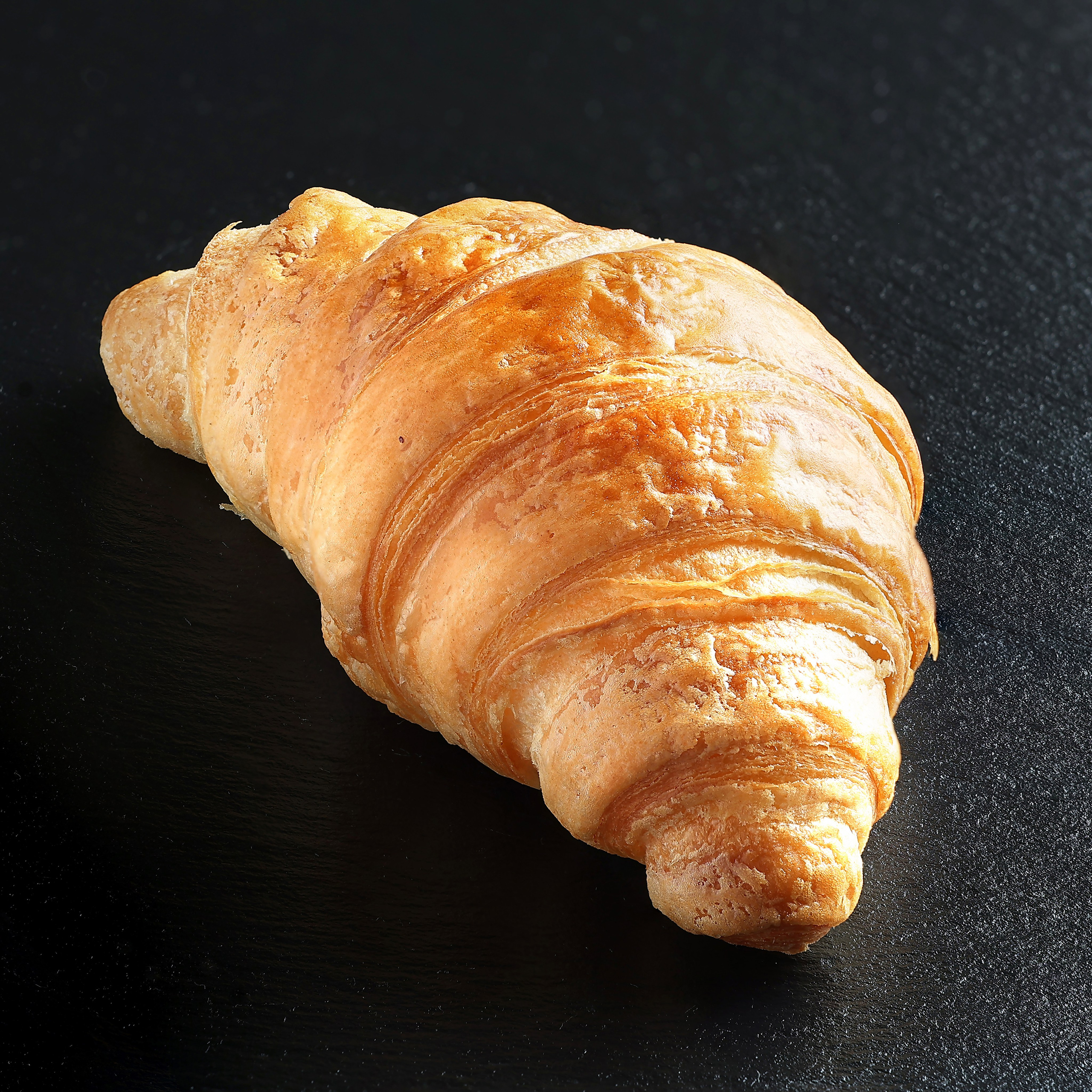 Свежий слоёный круассан крупным планом на темном фоне.