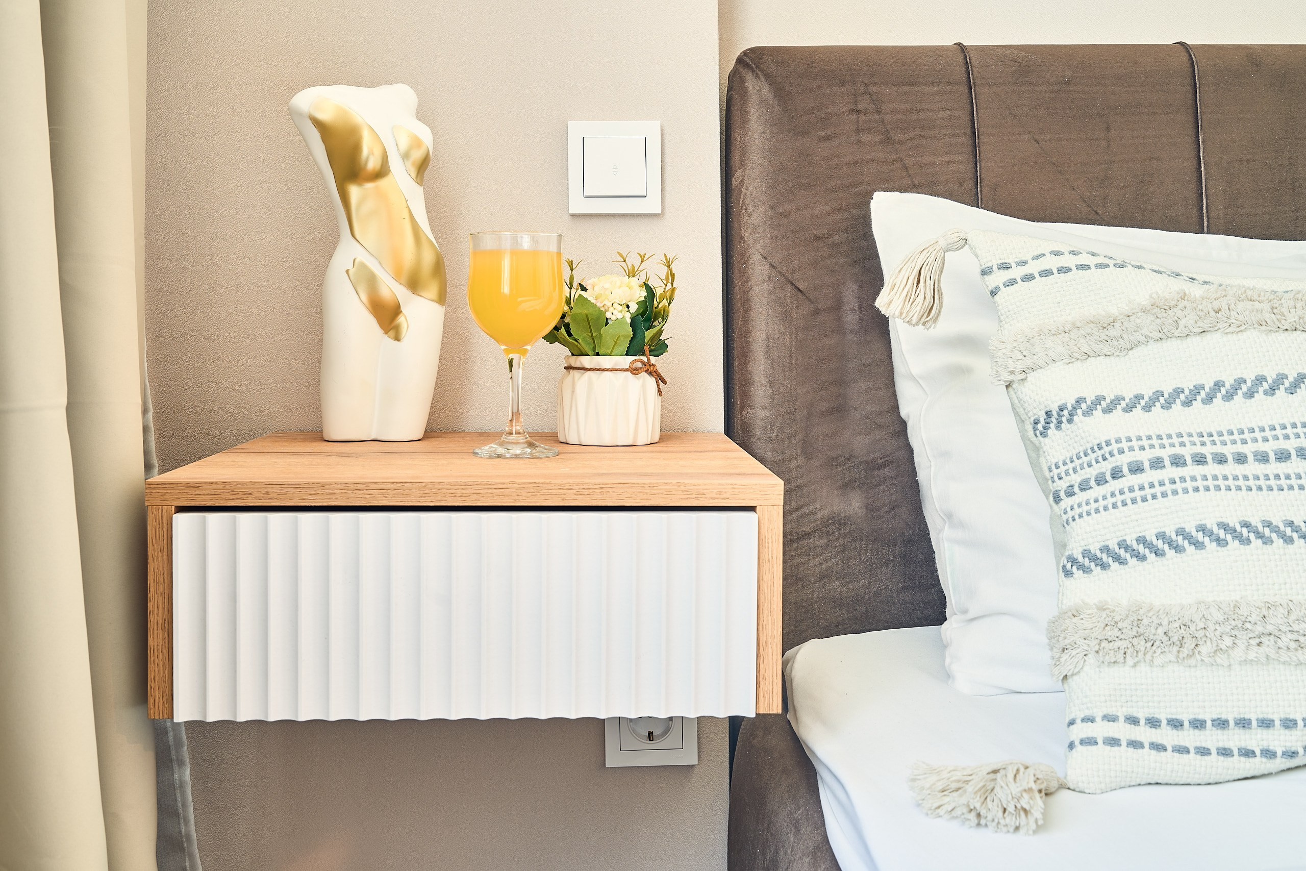 Интерьерная фотография с кроватью и прикроватной тумбочкой. Мягкая подушка и свежевыжатый сок