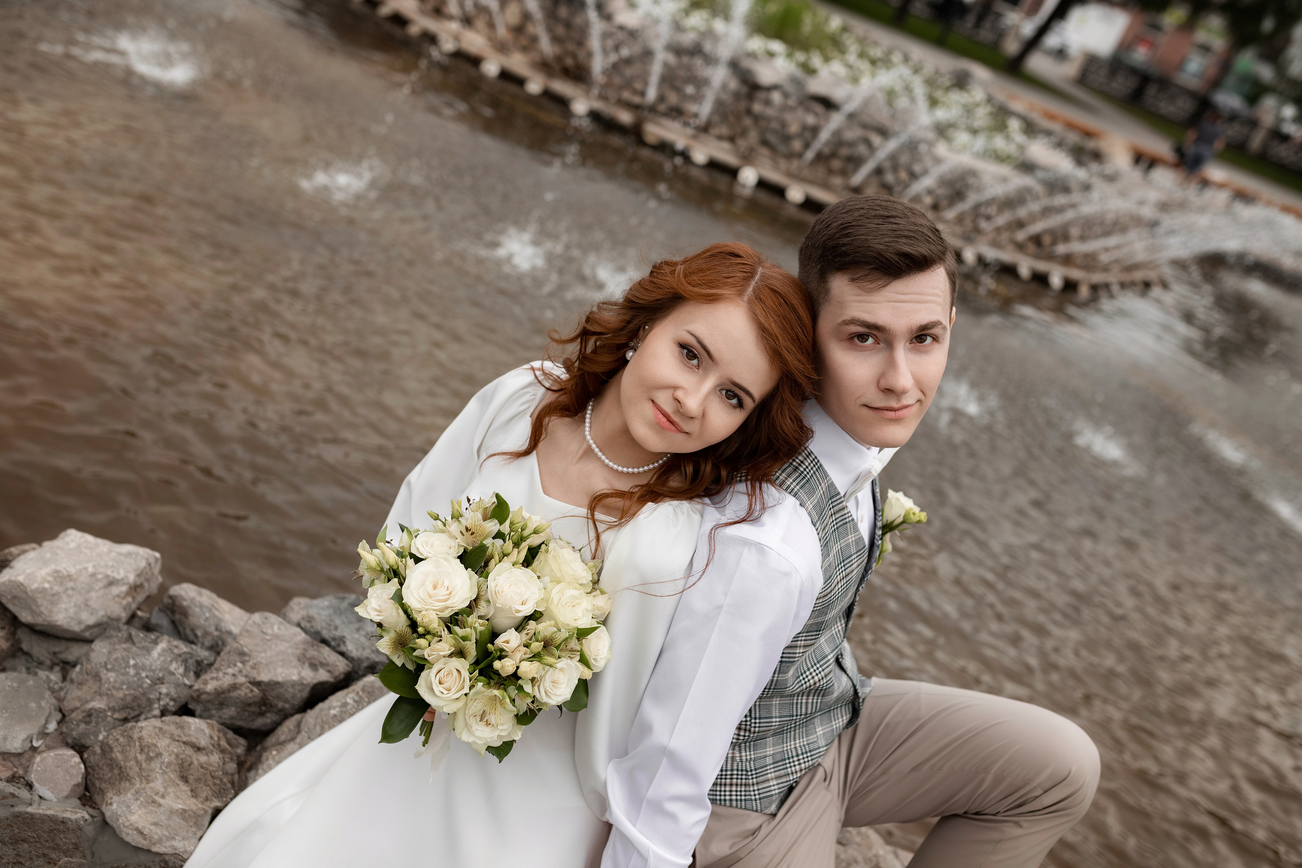 Невеста и жених в брызгах фонтана с букетом