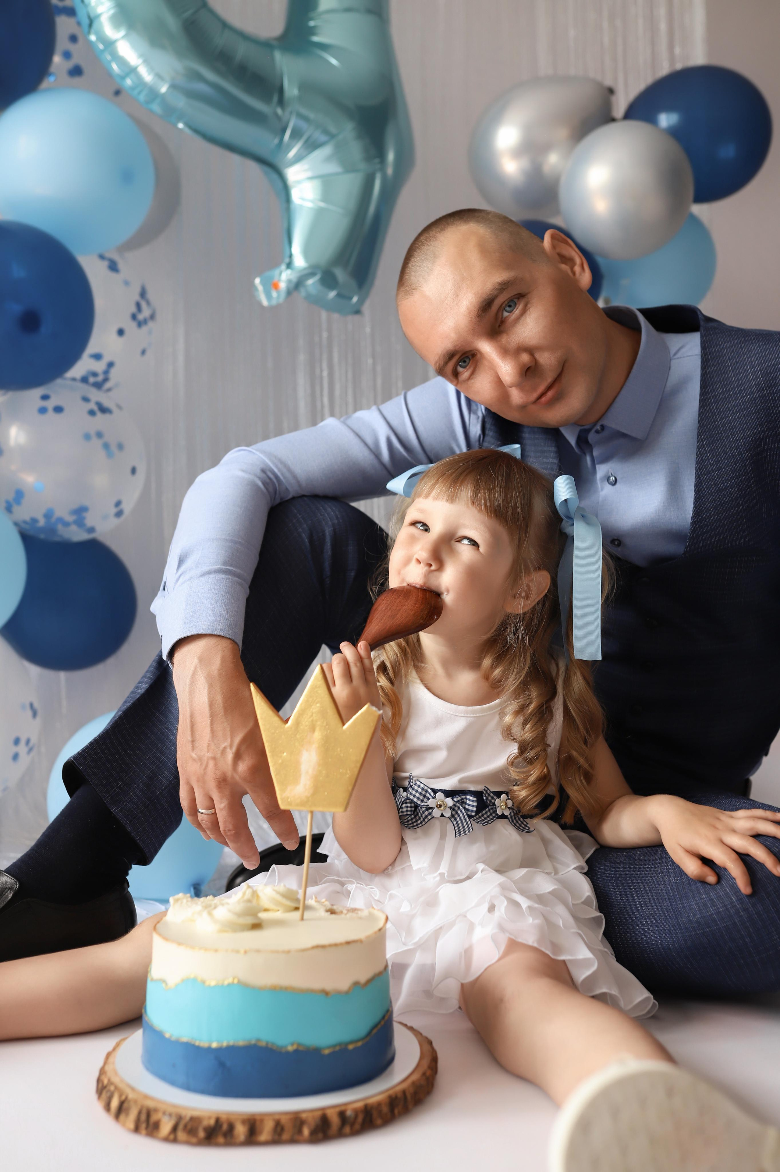 фотосессия на день рождения дочке с шариками тортом в белом платье с большими конфетами и большой ложкой. С папой.