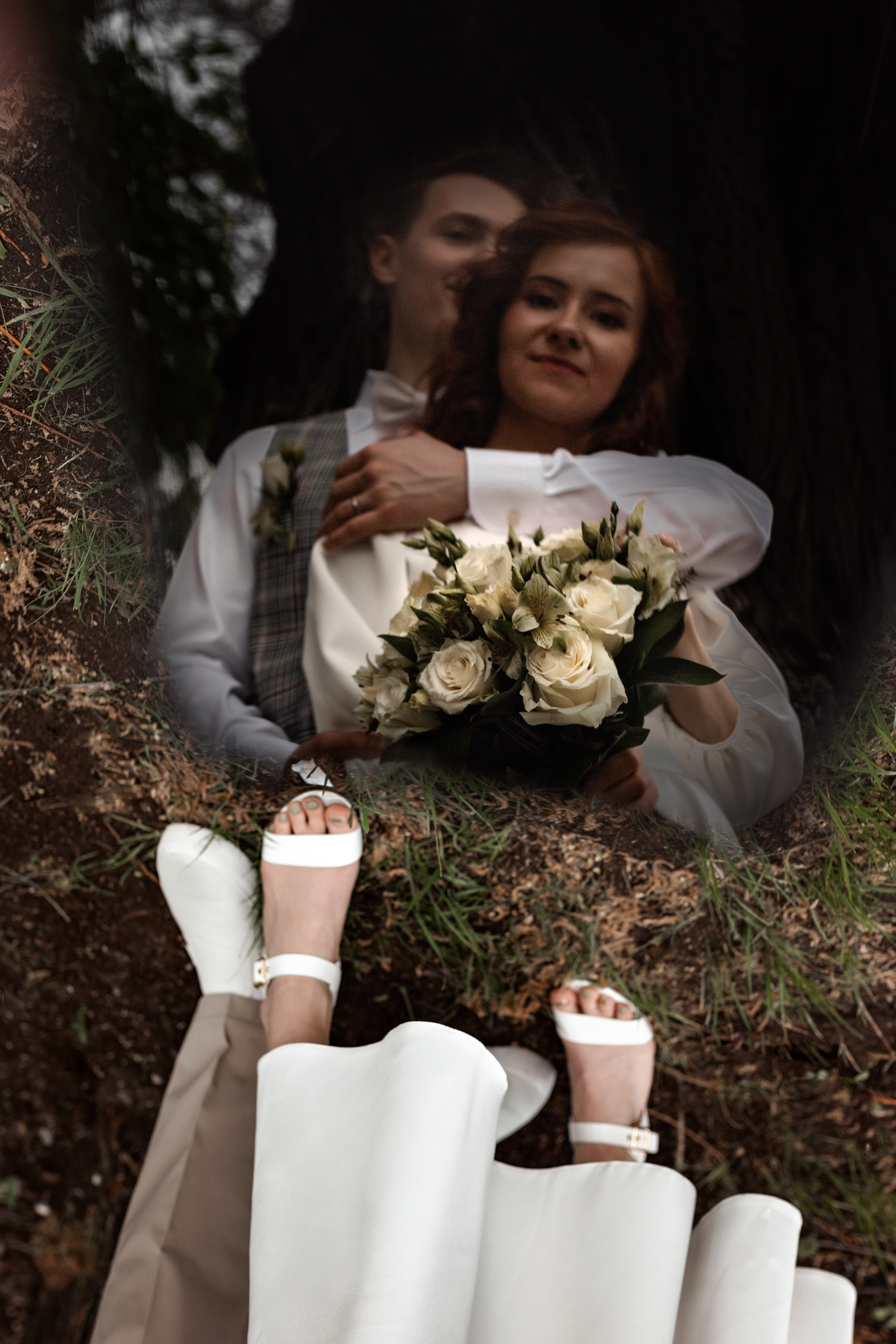 Молодожены на свадебной фото прогулке целуются у широкого ствола дерева