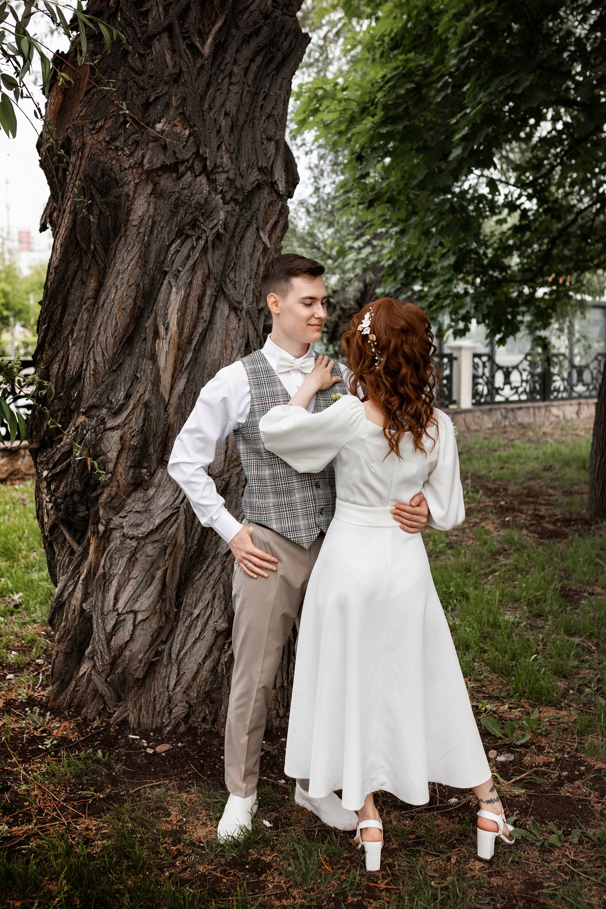 Молодожены на свадебной фото прогулке целуются у широкого ствола дерева