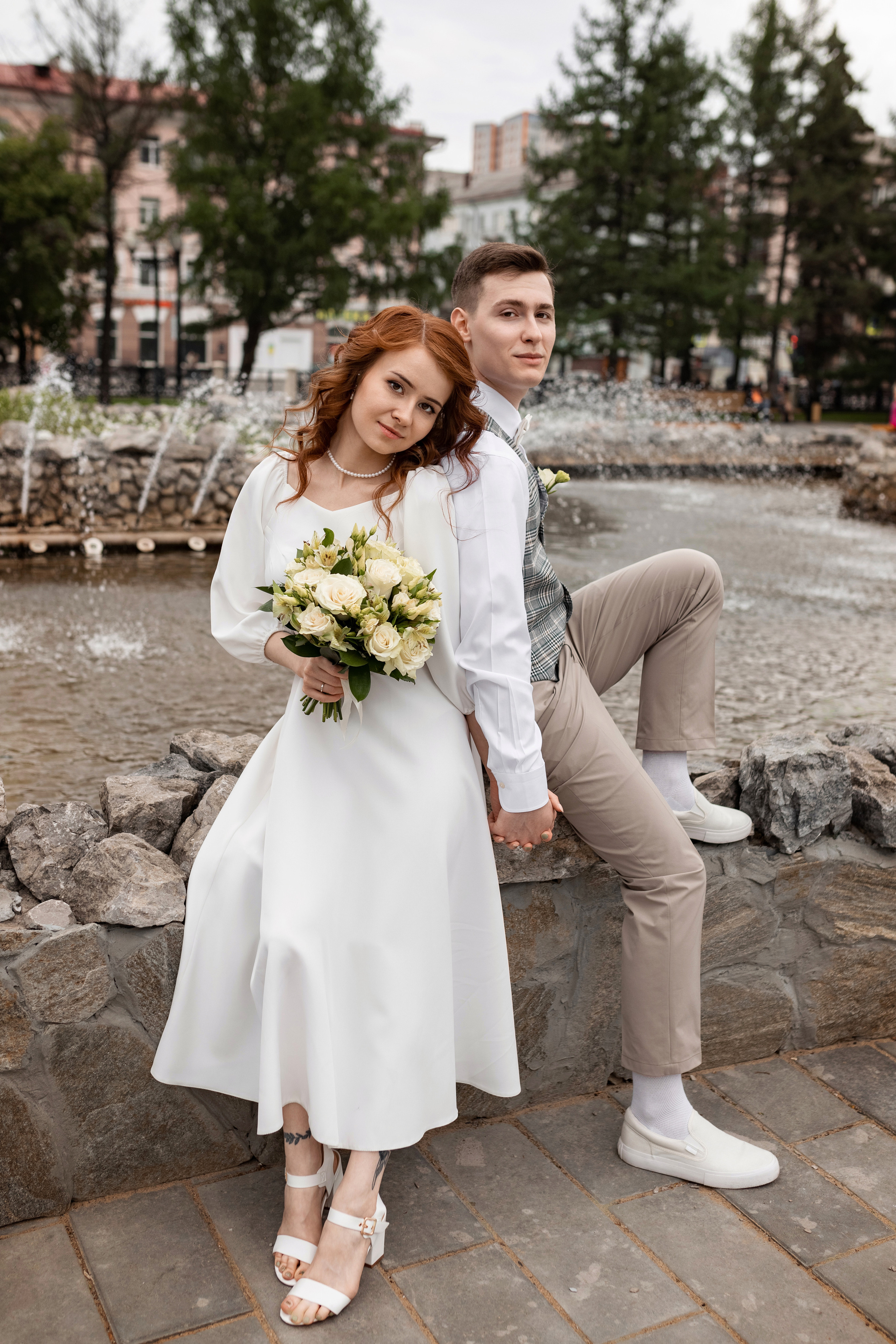 Невеста и жених в брызгах фонтана с букетом