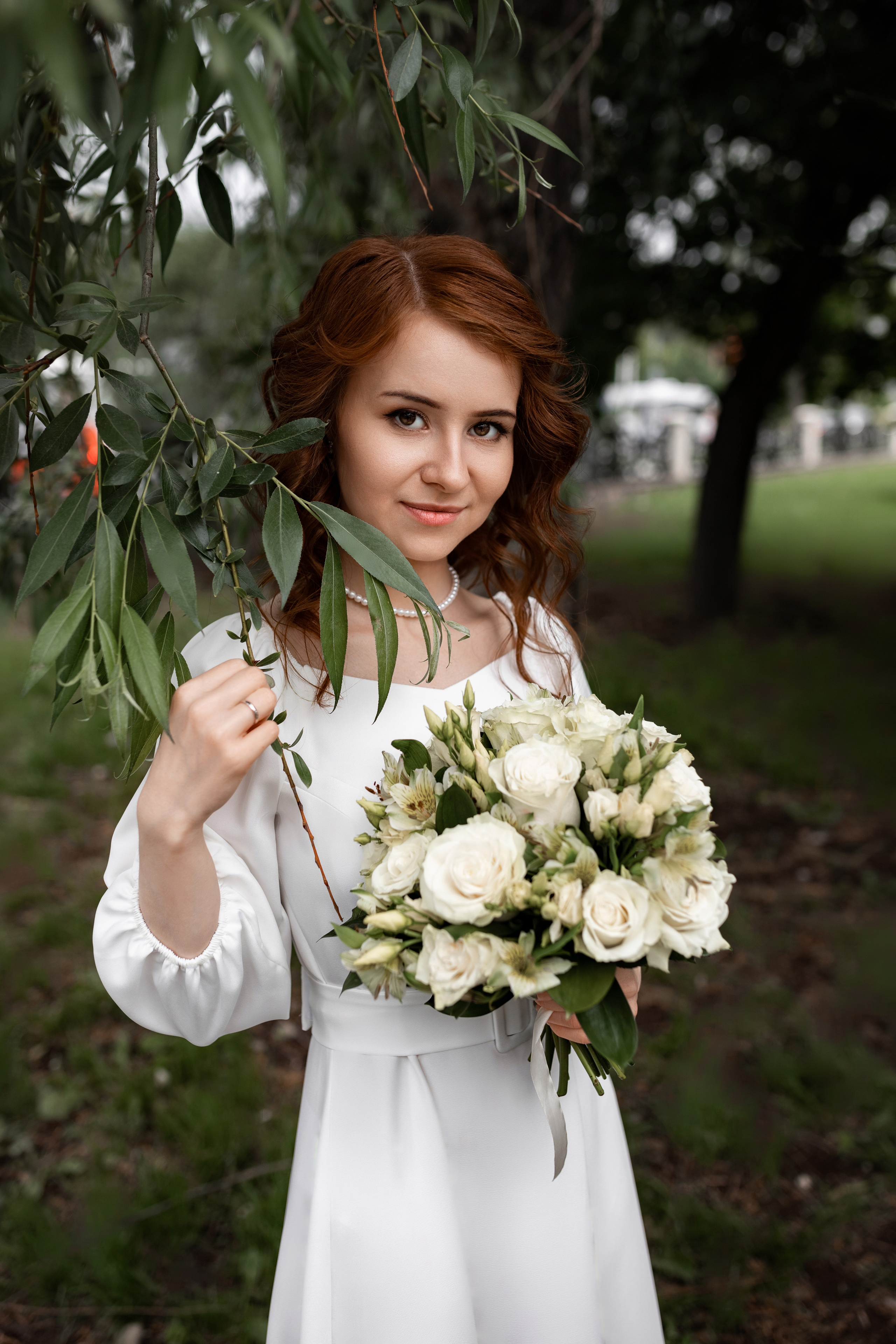 невеста позирует с букетом в листьях дерева
