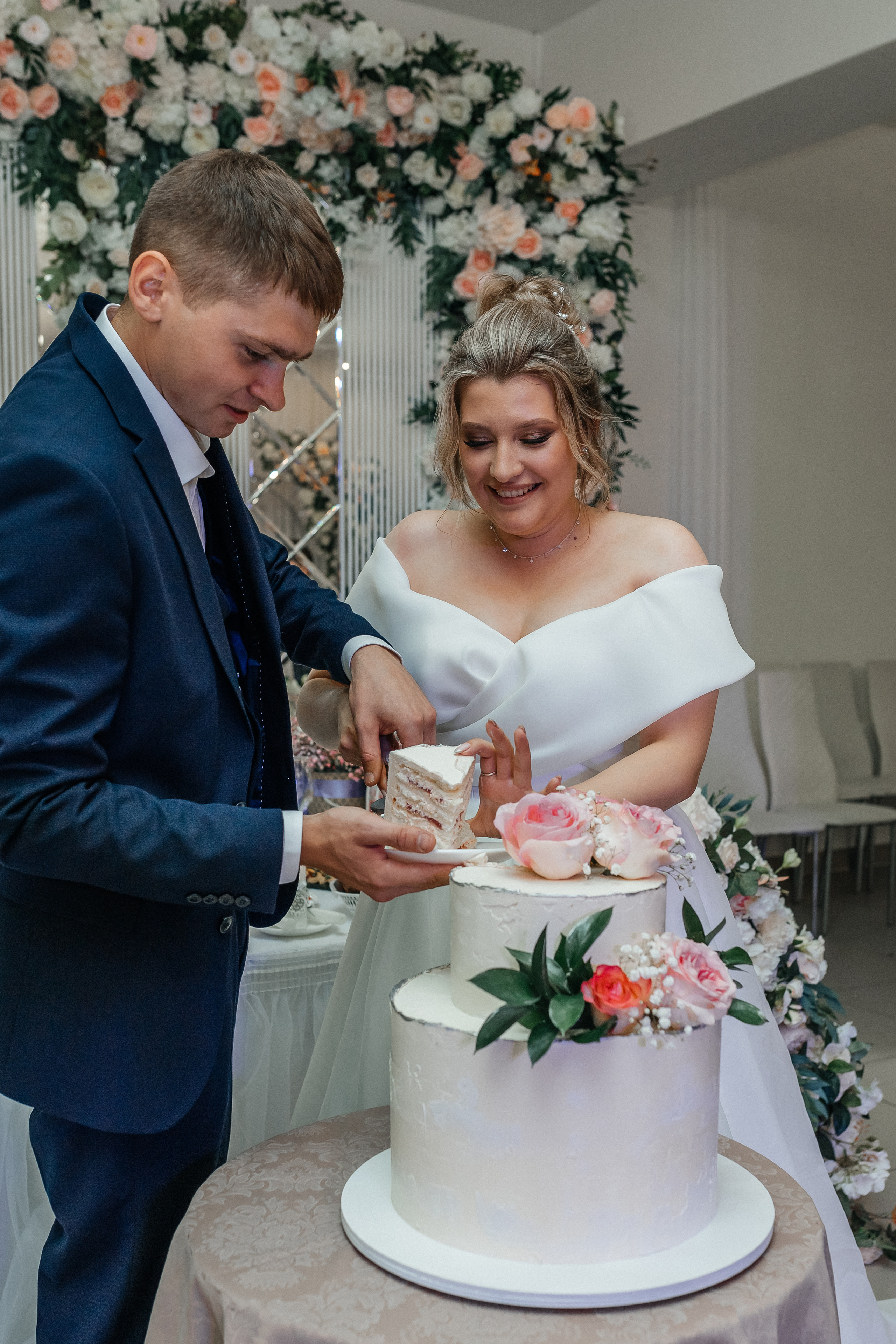 жених и невеста режут свадебный торт с живыми цветами