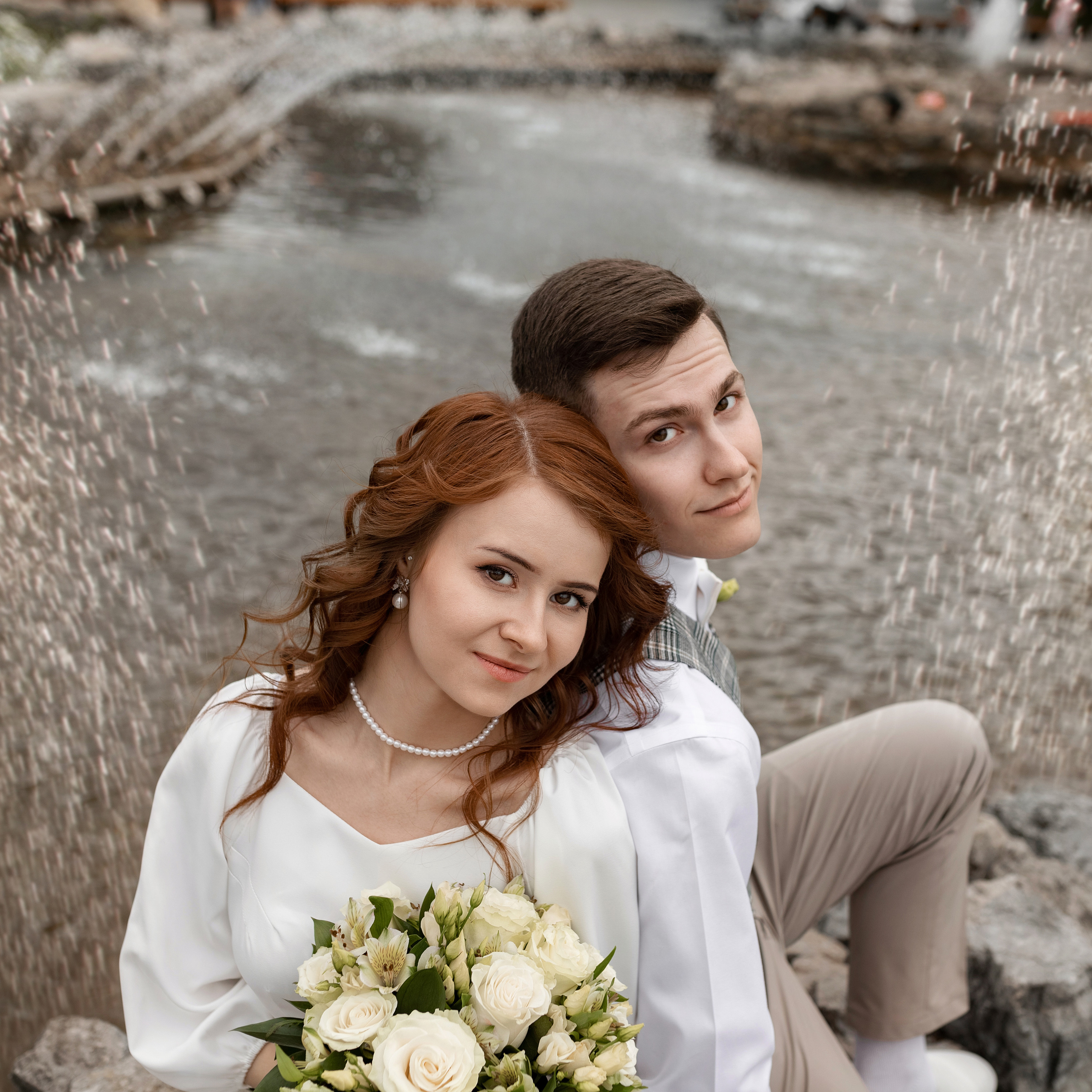 Невеста и жених в брызгах фонтана с букетом