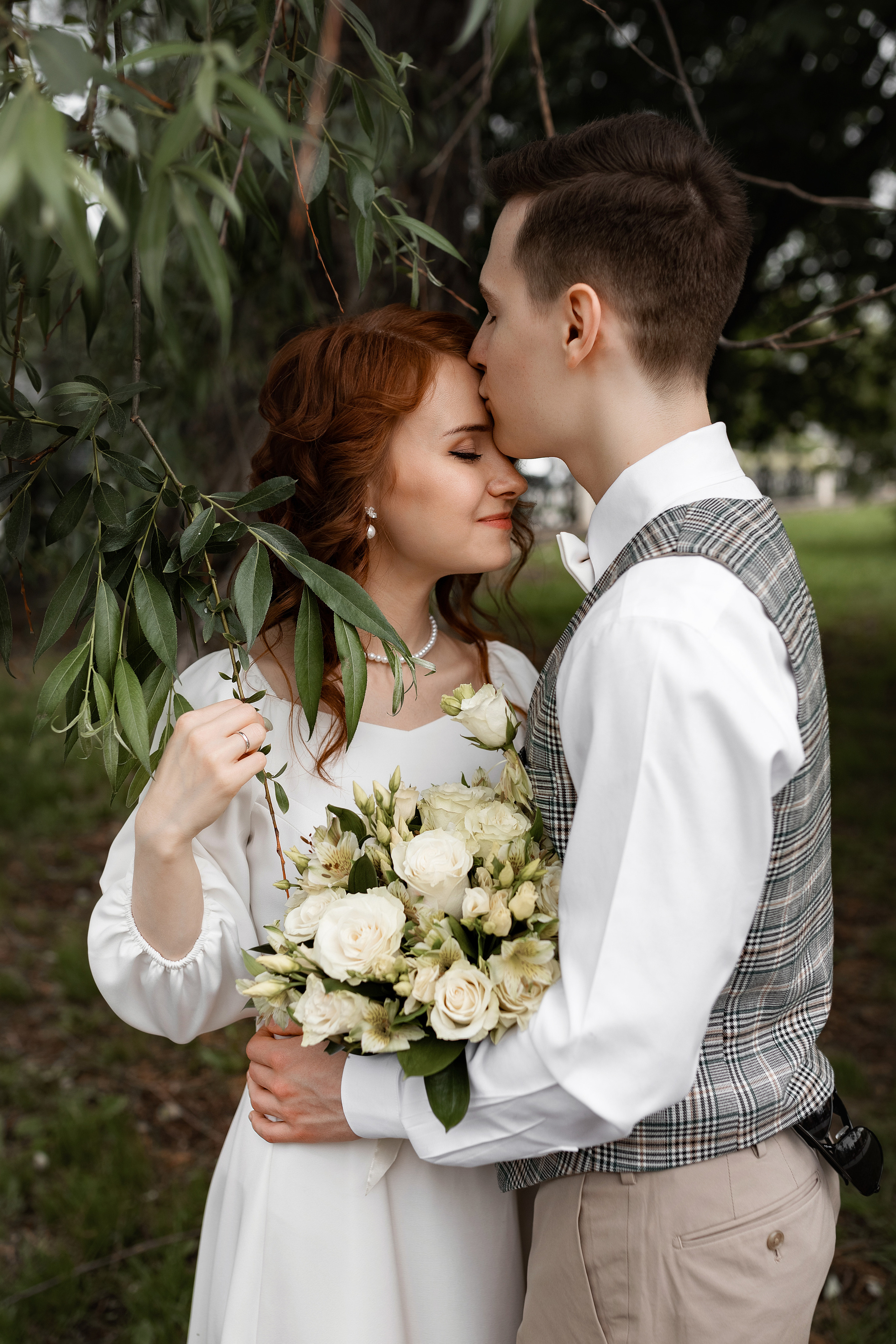 невеста позирует с букетом в листьях дерева