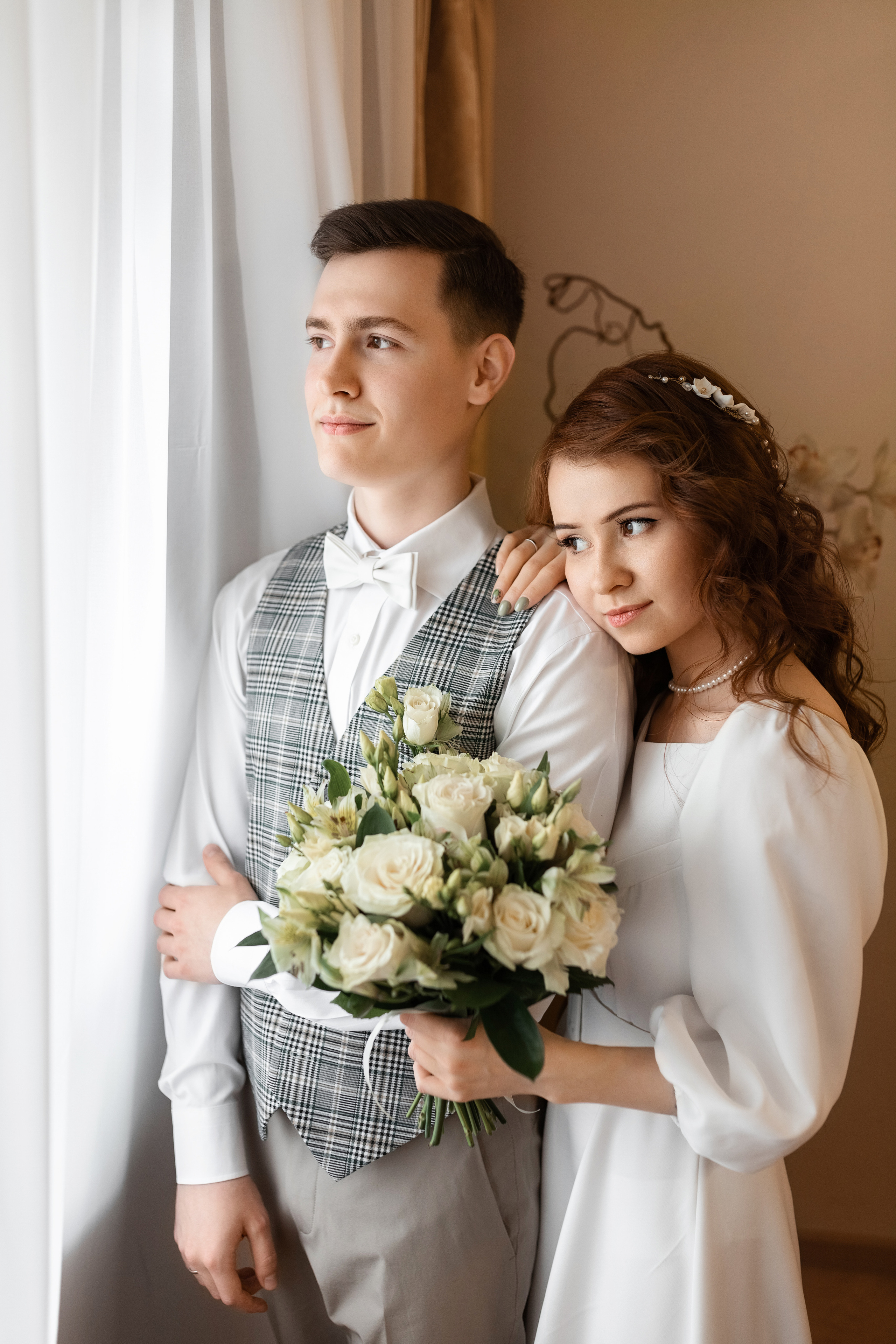 Молодожены стоят у окна в ЗАГСе