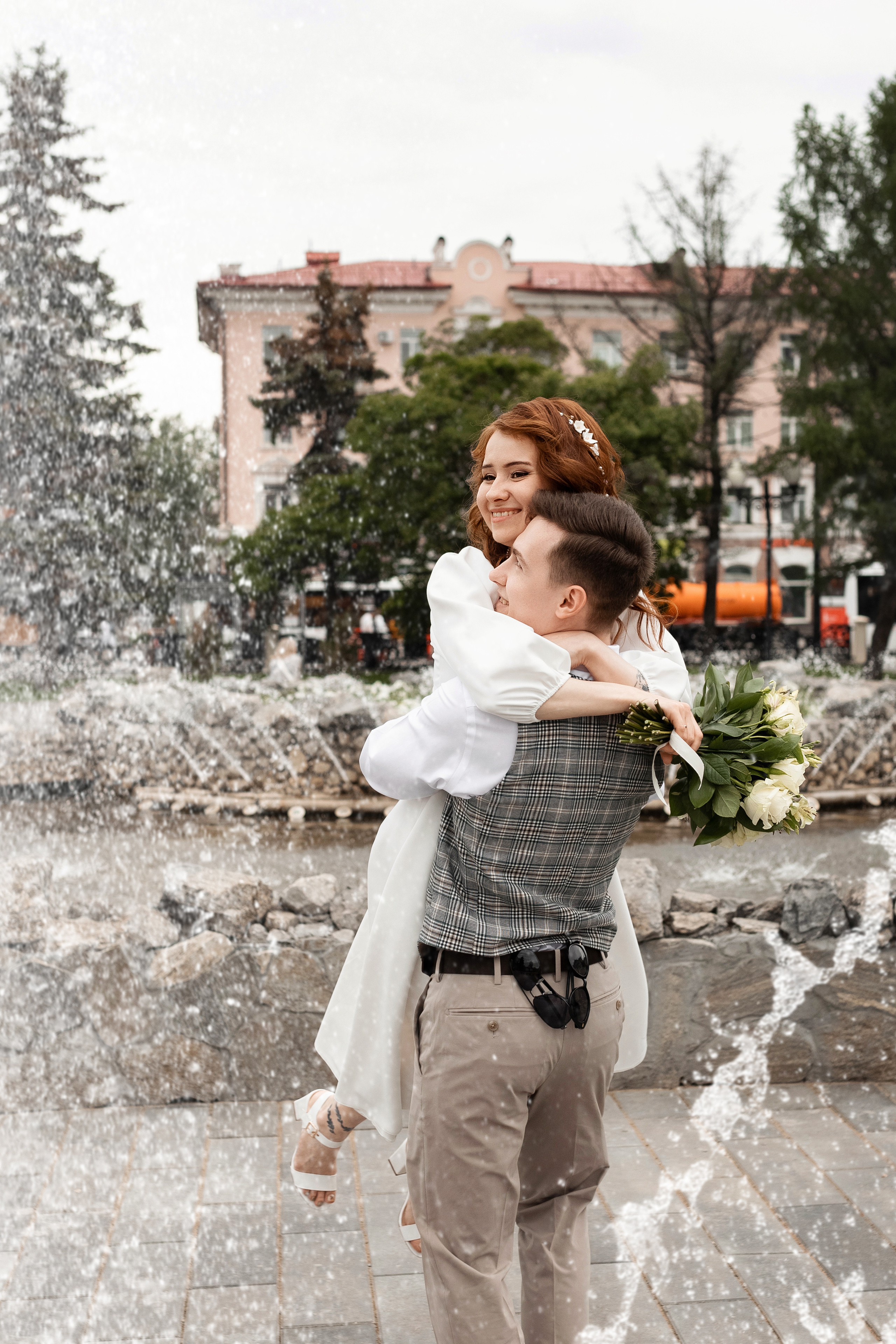 Невеста и жених кружатся в брызгах фонтана с букетом