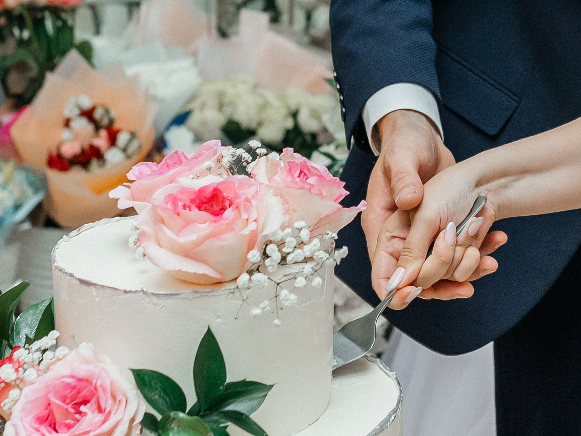 жених и невеста режут свадебный торт с живыми цветами