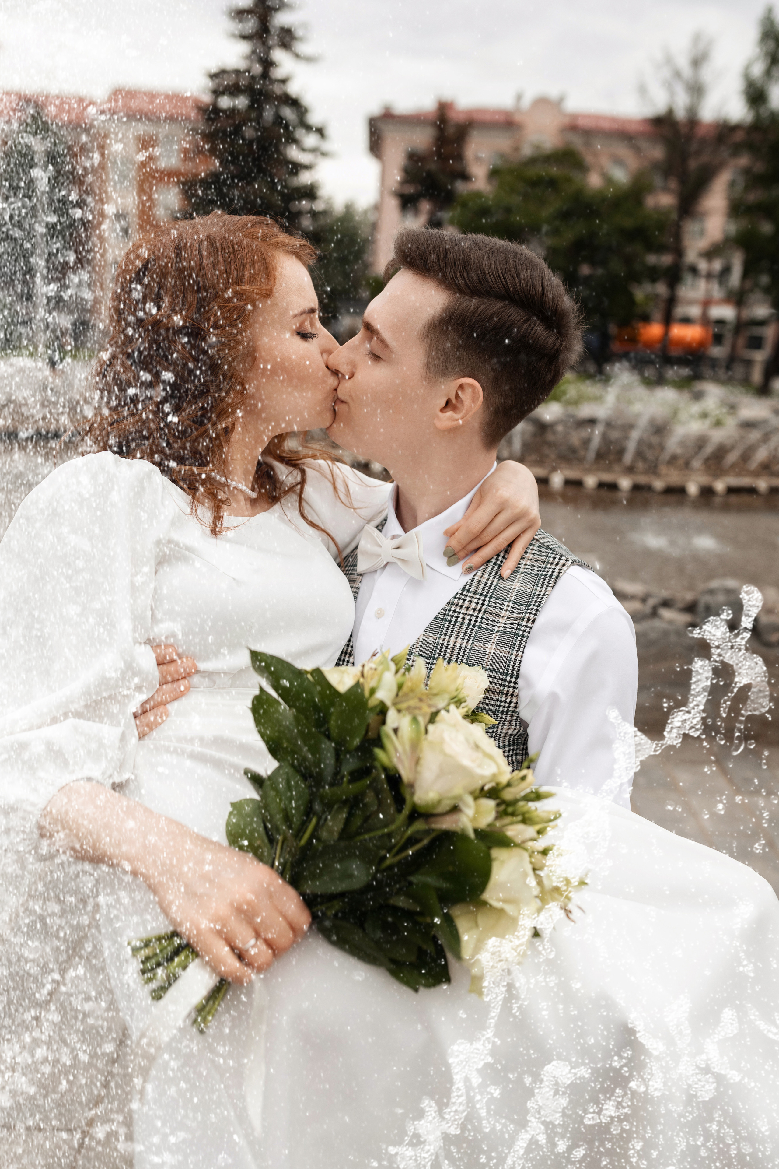 Невеста и жених кружатся в брызгах фонтана с букетом