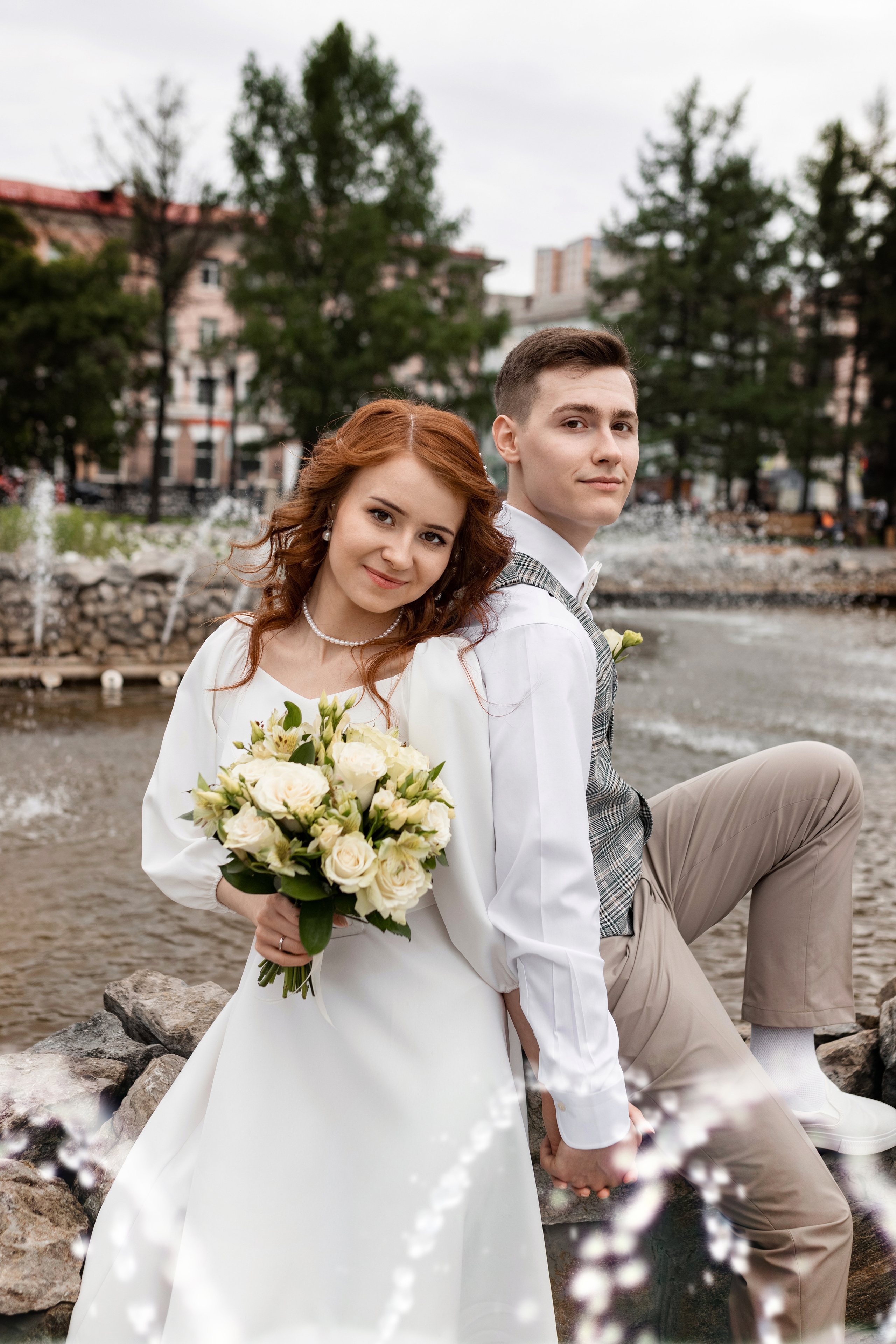 Невеста и жених в брызгах фонтана с букетом