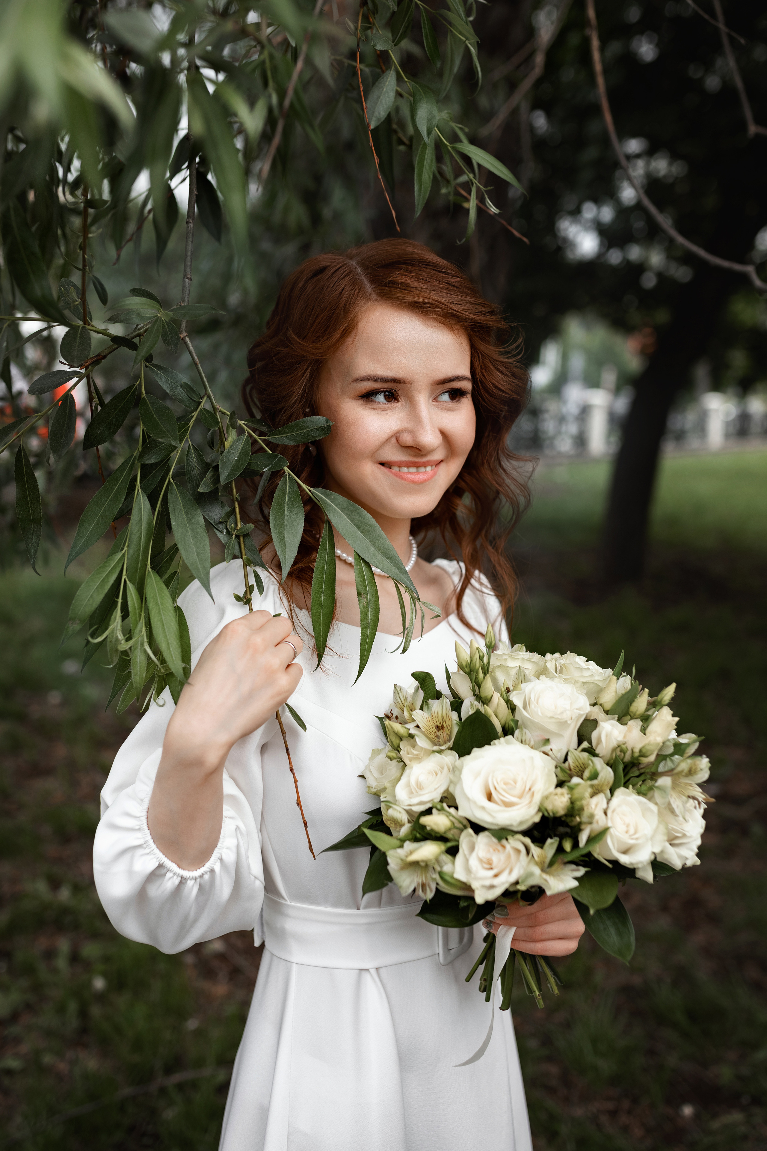 невеста позирует с букетом в листьях дерева