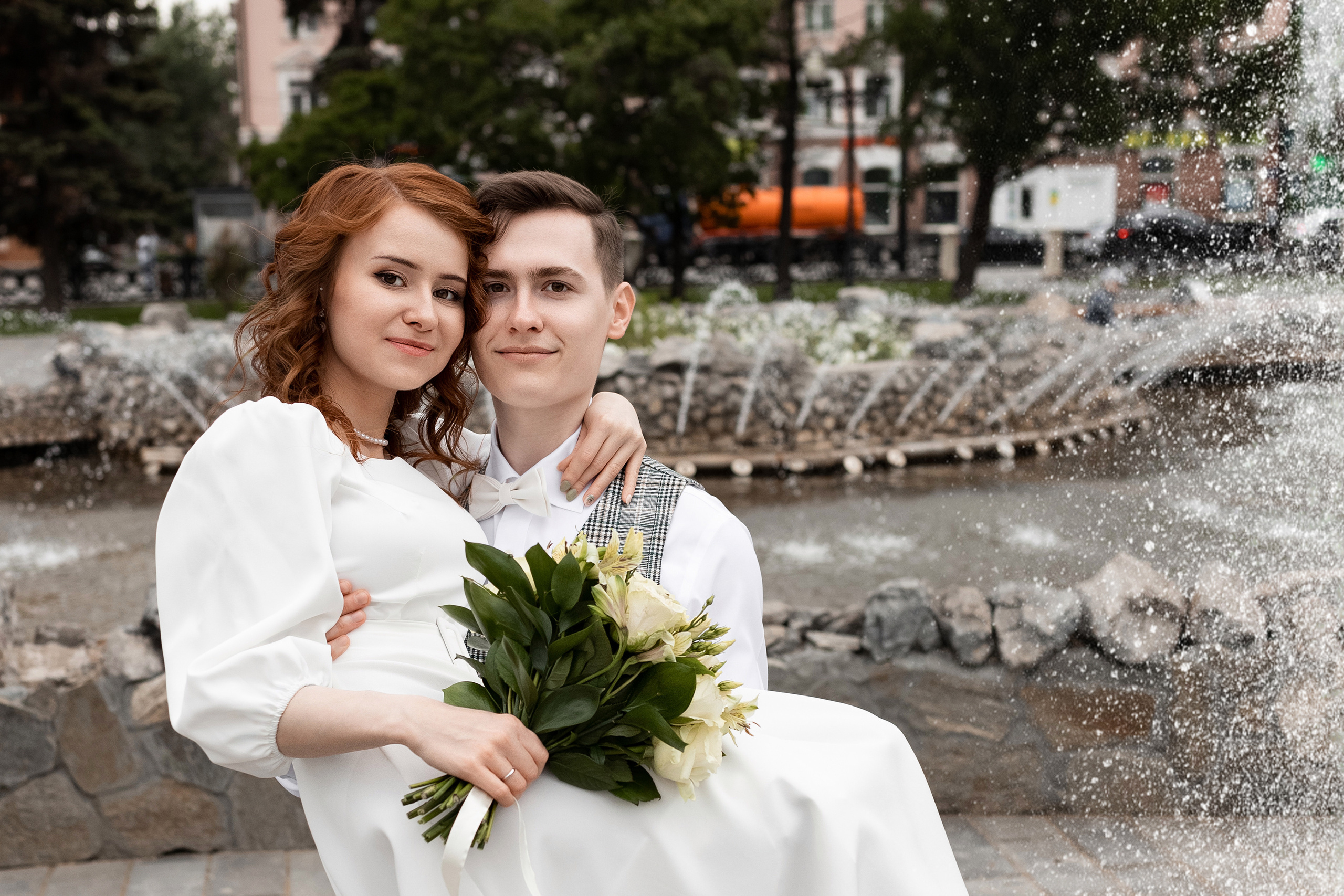 Невеста и жених кружатся в брызгах фонтана с букетом