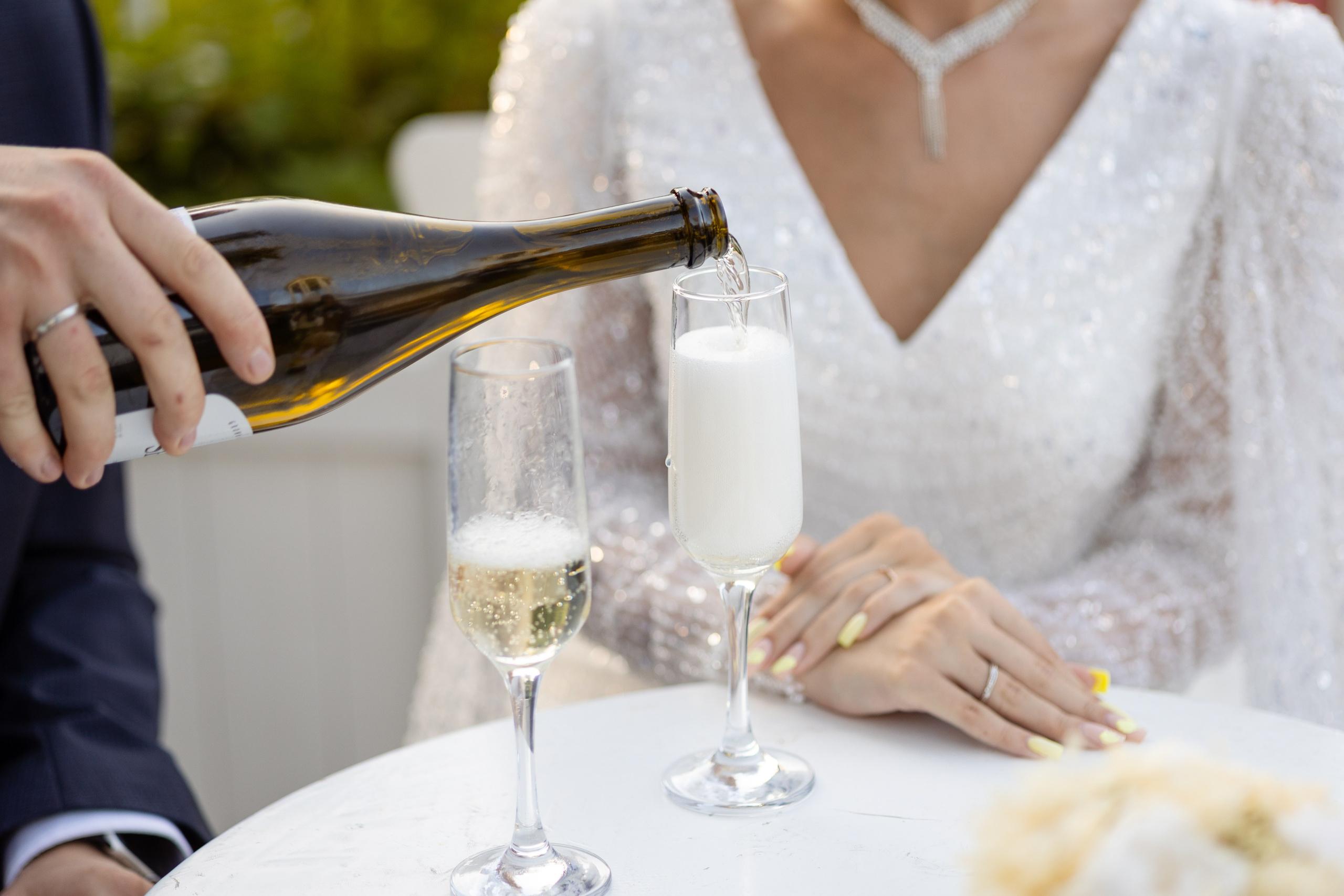 Сидящей за столом молодой наливают в бокал шампанское.