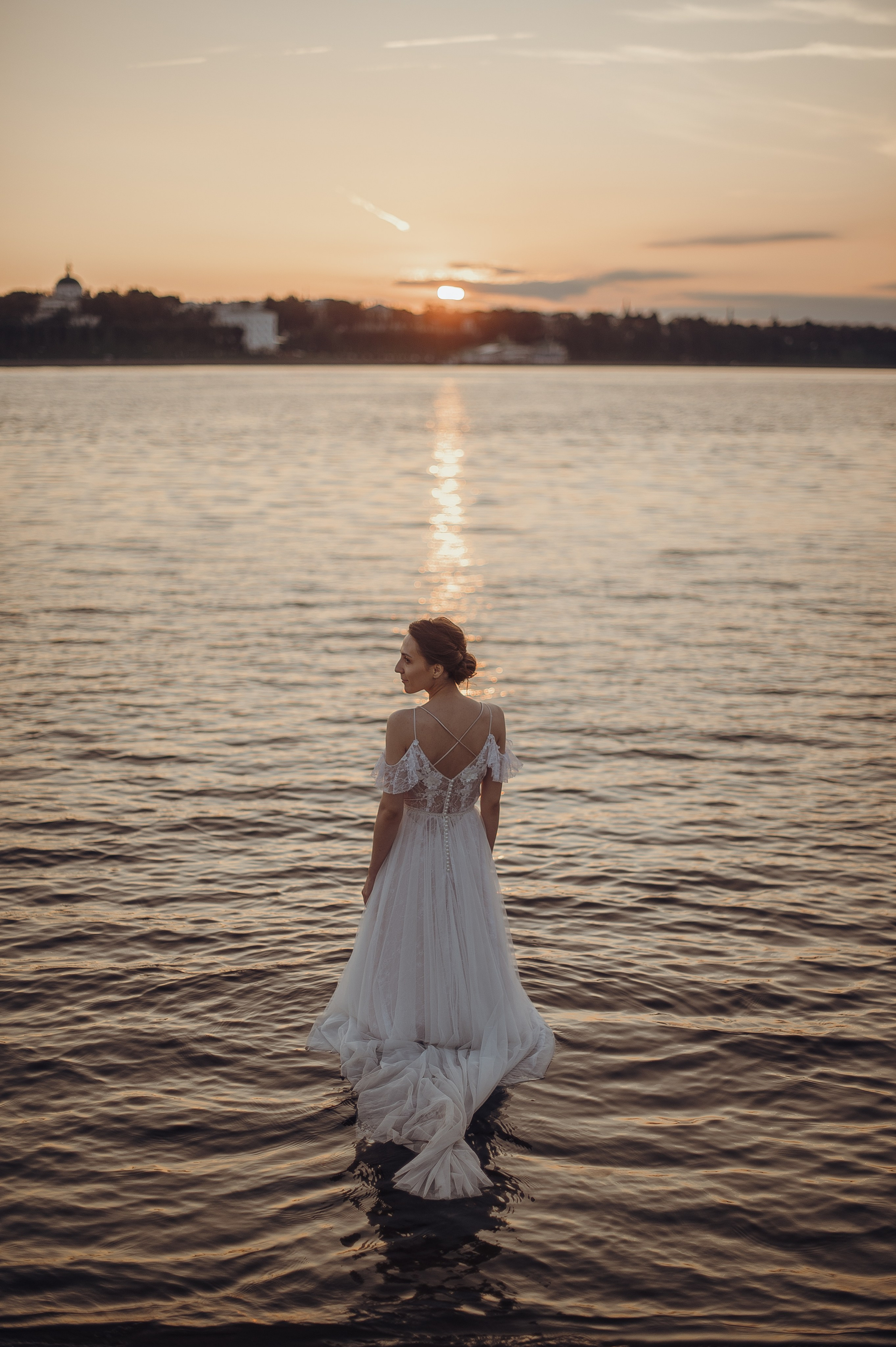 Невеста красиво заходит в воду в свадебном платье на закате