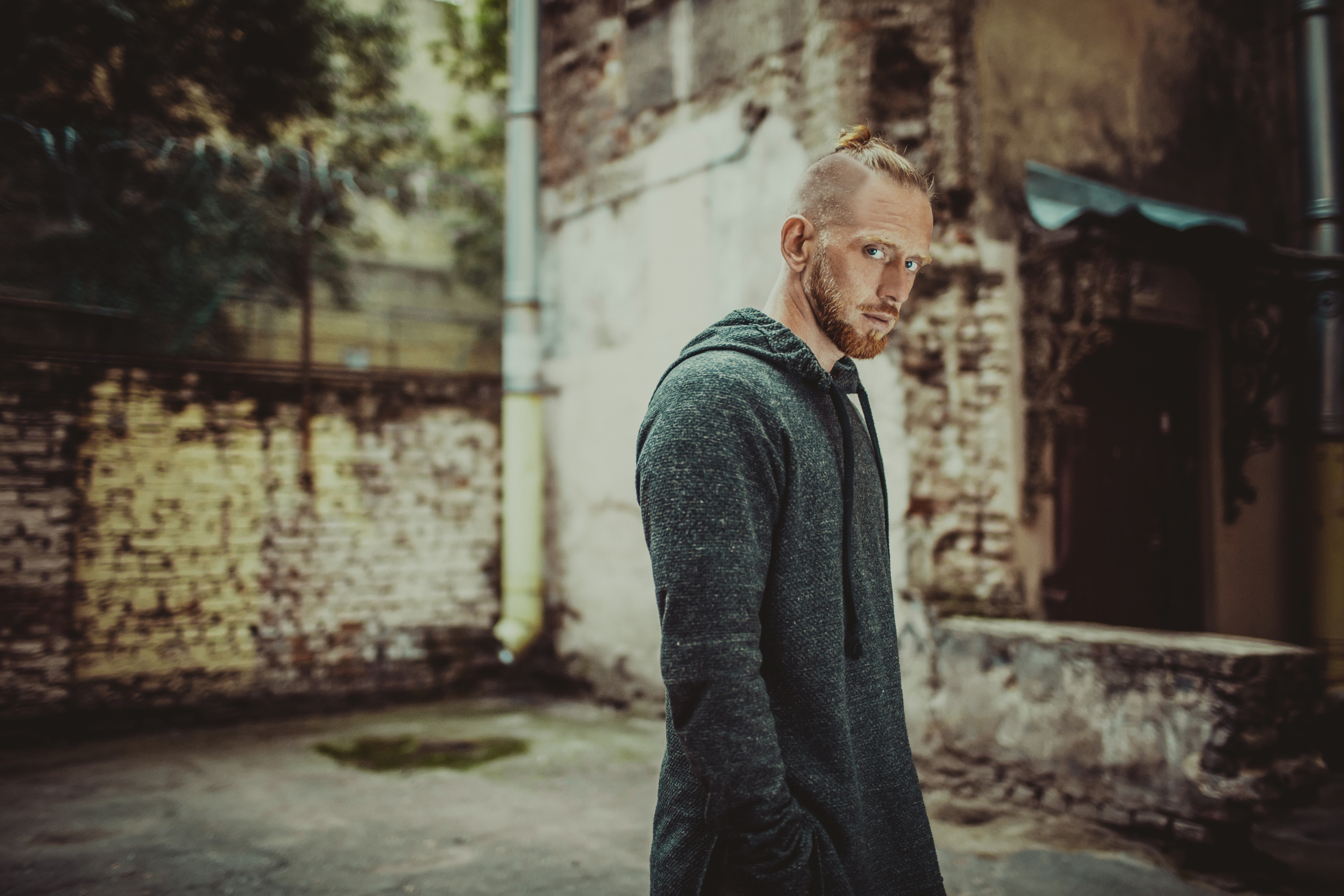 рыжий мужчина в сером худи в кирпичном дворе