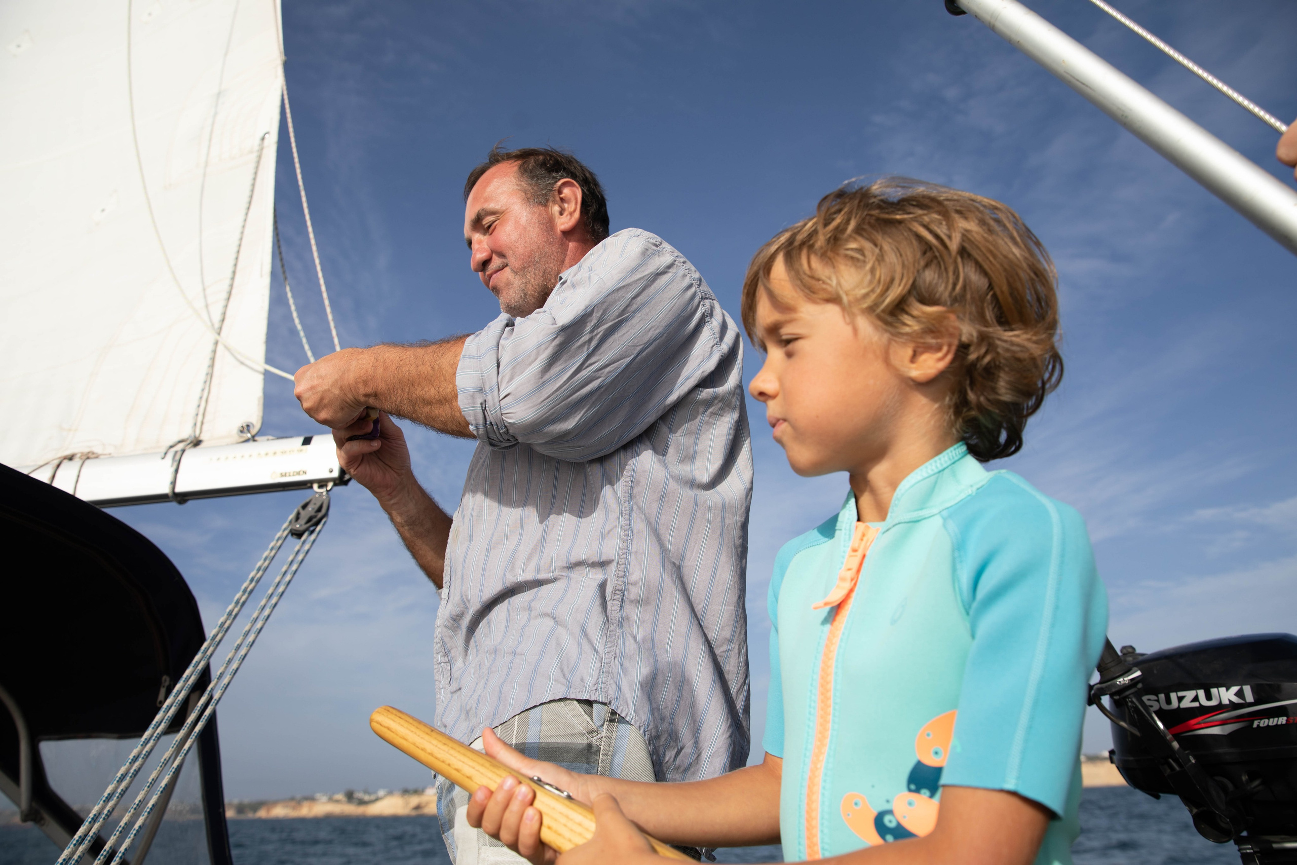 Families with children are photographed during a sailing yacht trip in the Algarve. Boys in lifejackets steer a sailing yacht and watch birds and dolphins through binoculars.