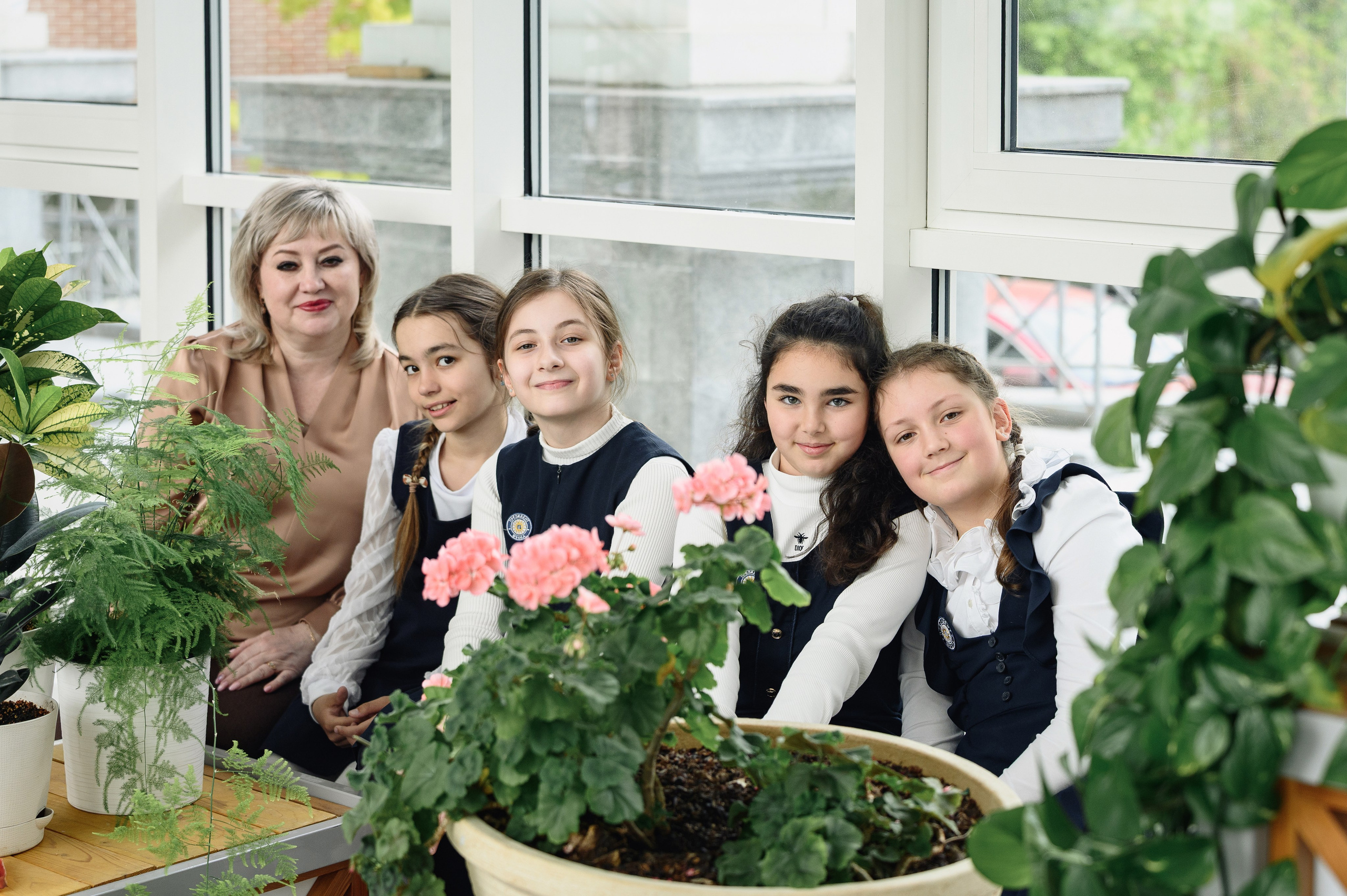 Группа школьниц с учительницей позирует среди растений в коридоре