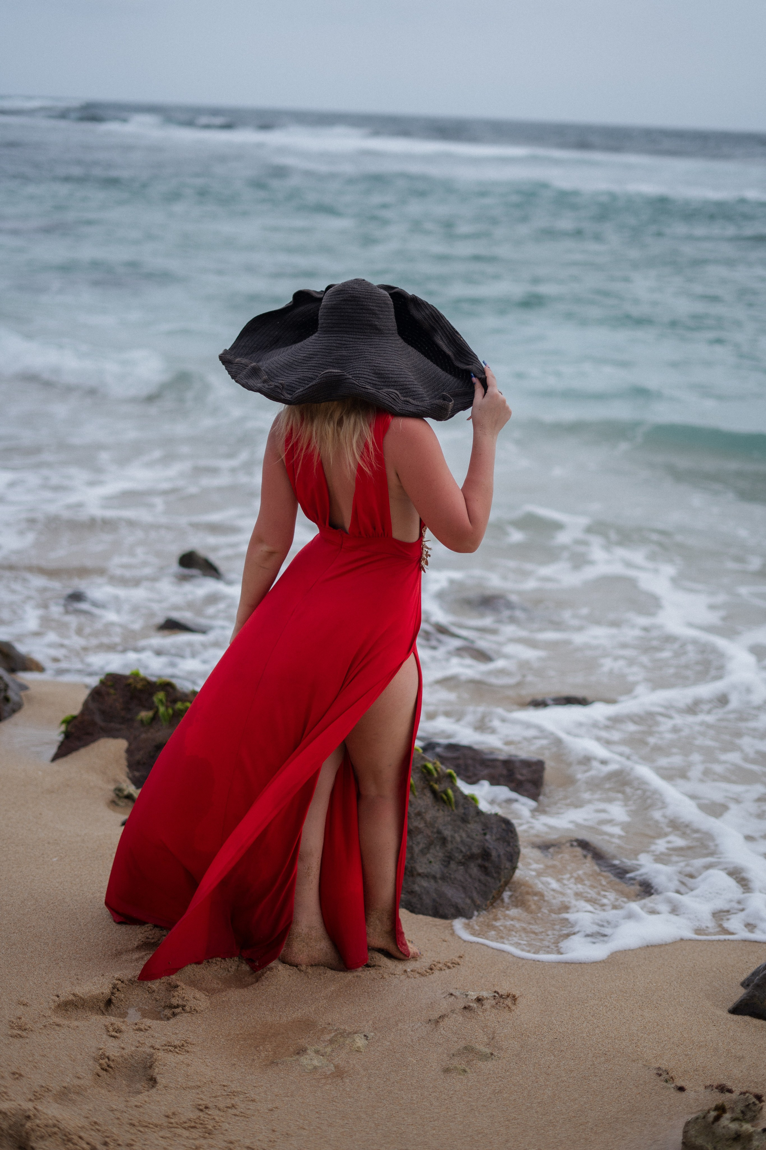 a blonde in a red dress sitting on the sand by the ocean
