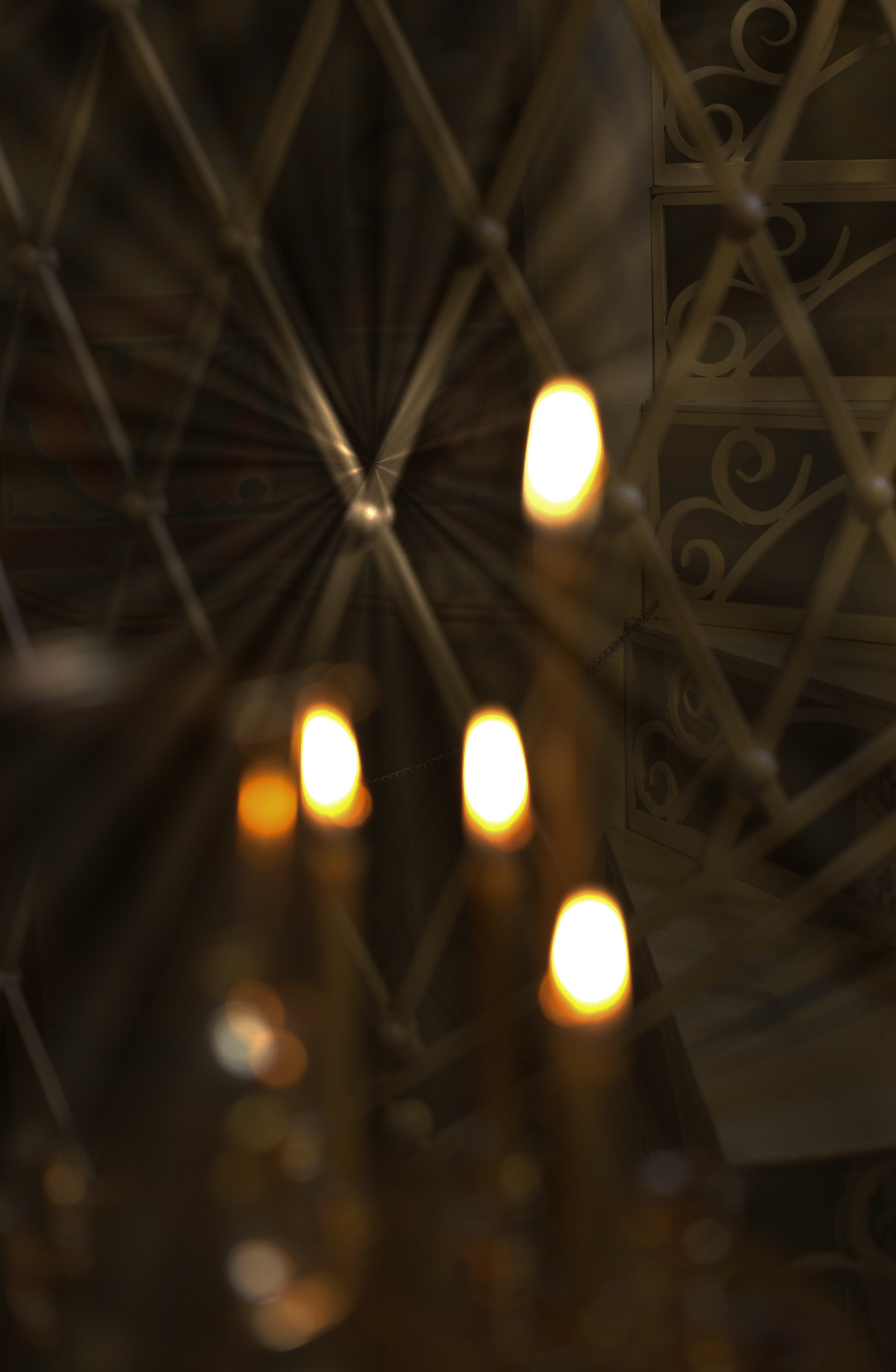 Горящие церковные свечи на фоне металлической решетки в храме