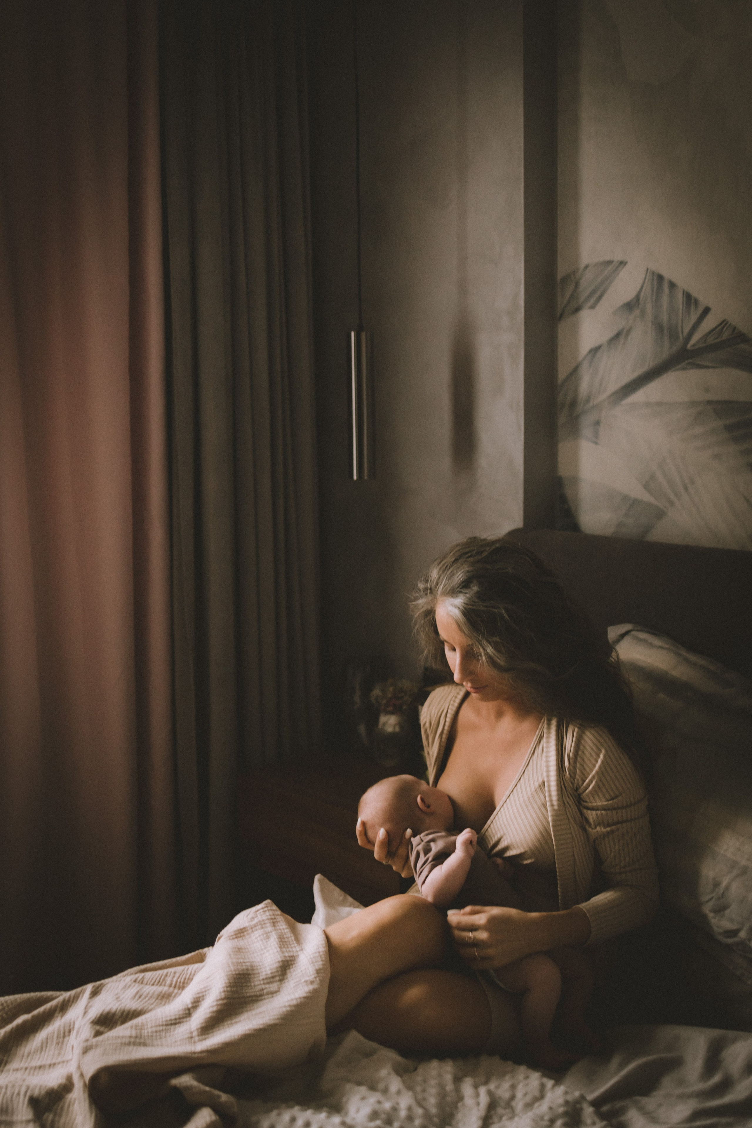мама кормит младенца, сидя на кровати в уютной домашней атмосфере