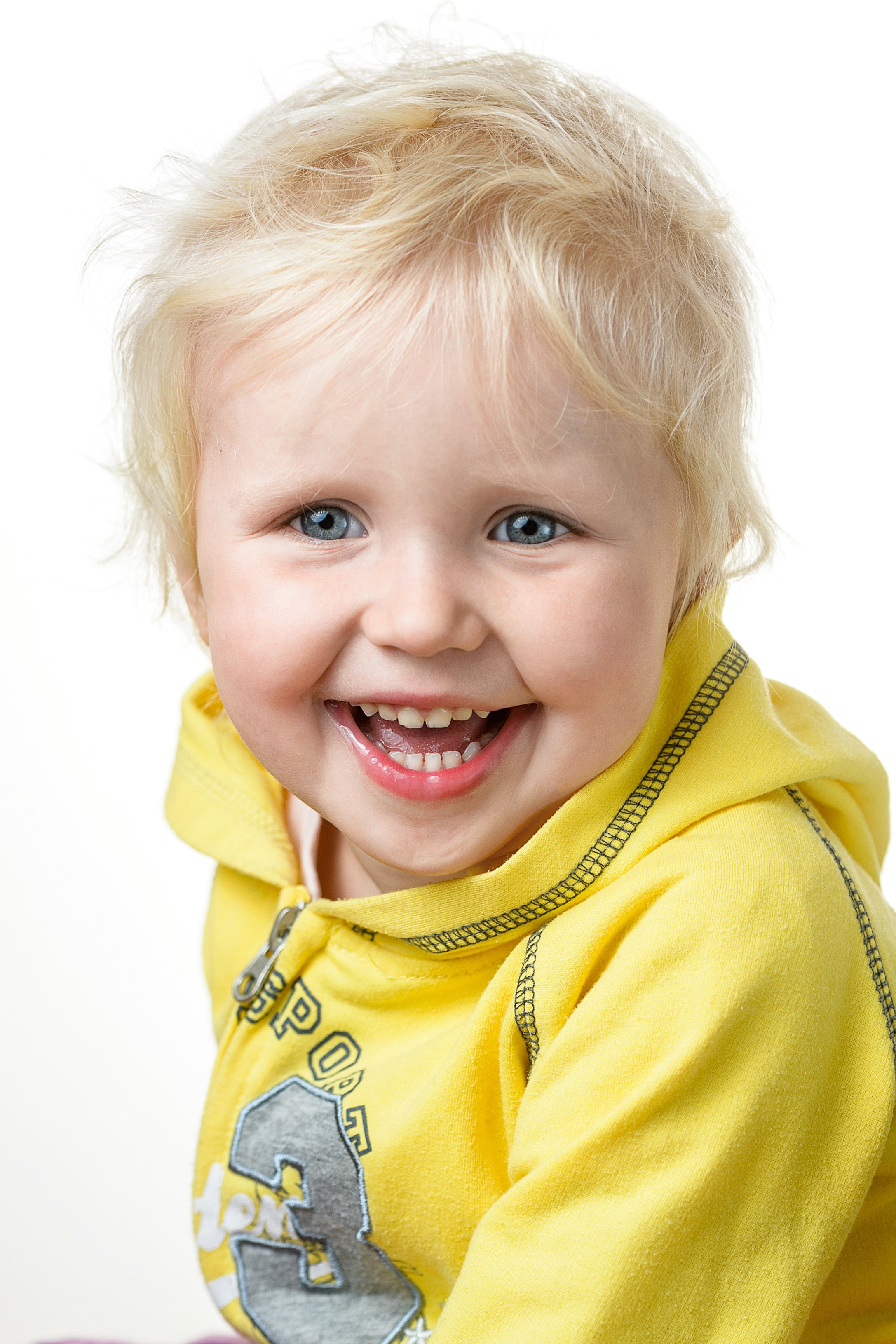 Светловолосая девочка в жёлтой толстовке улыбается в ярком портрете на белом фоне.