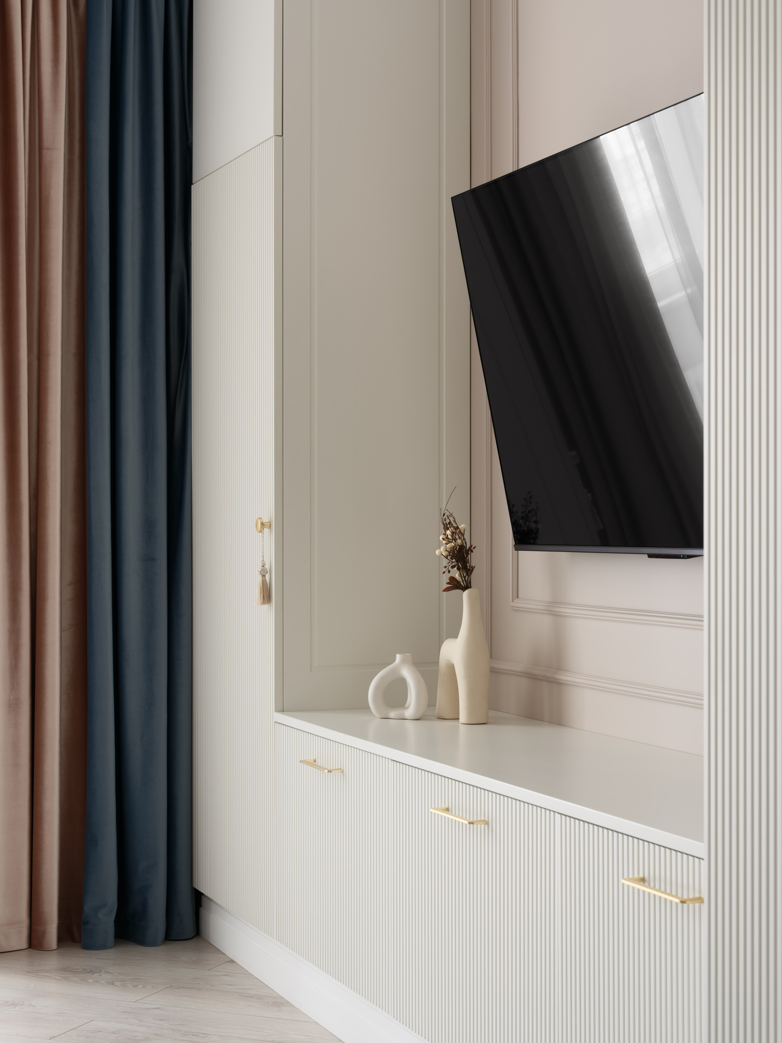 Современная зона ТВ с белыми рифлеными фасадами, встроенными шкафами и акцентными шторами в бежево-синих тонах. На тумбе стильный декор. Интерьер от Евгении Ермошиной, фото Сергея Денисенко.