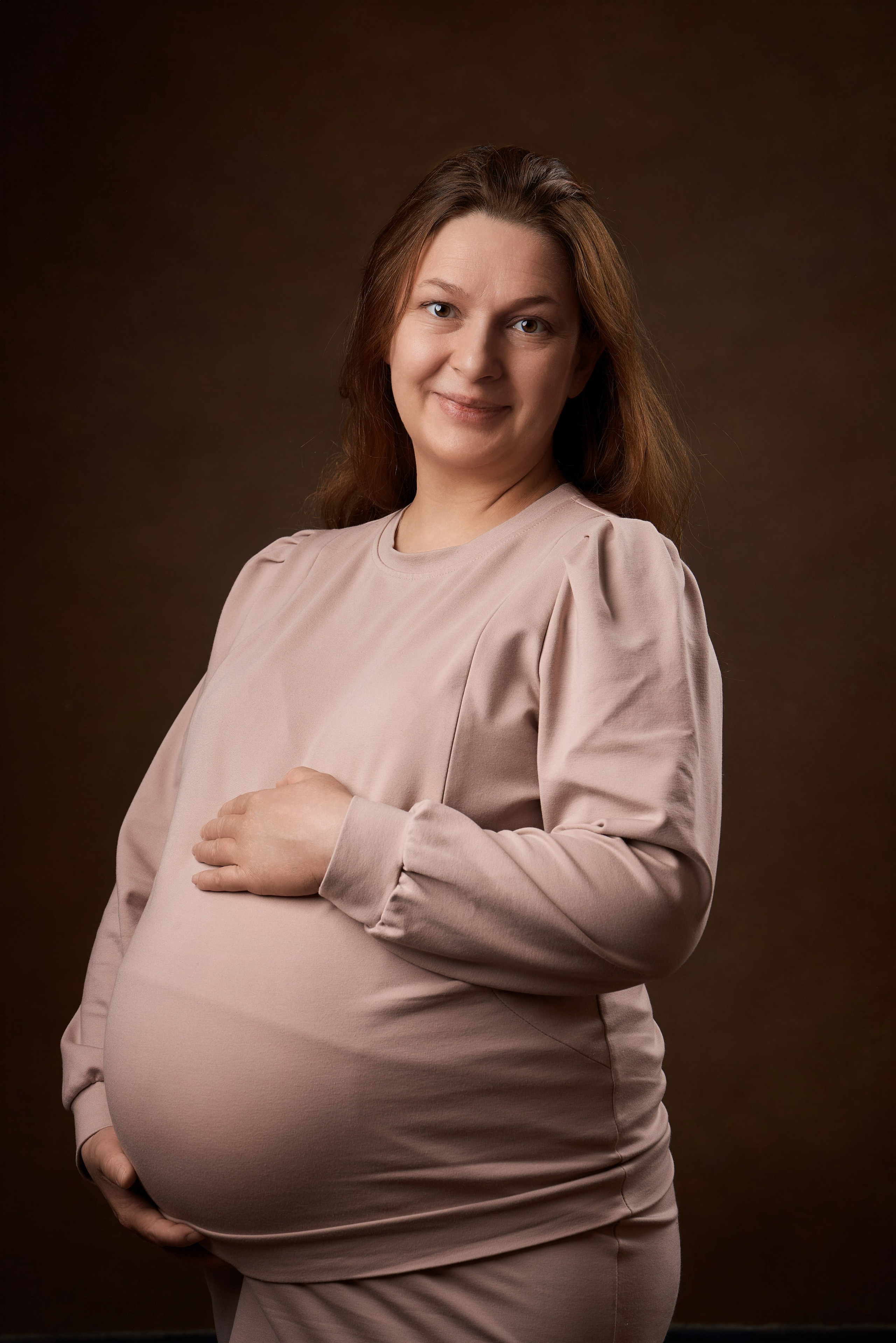 портрет беременной женщины в студии на коричневом фоне