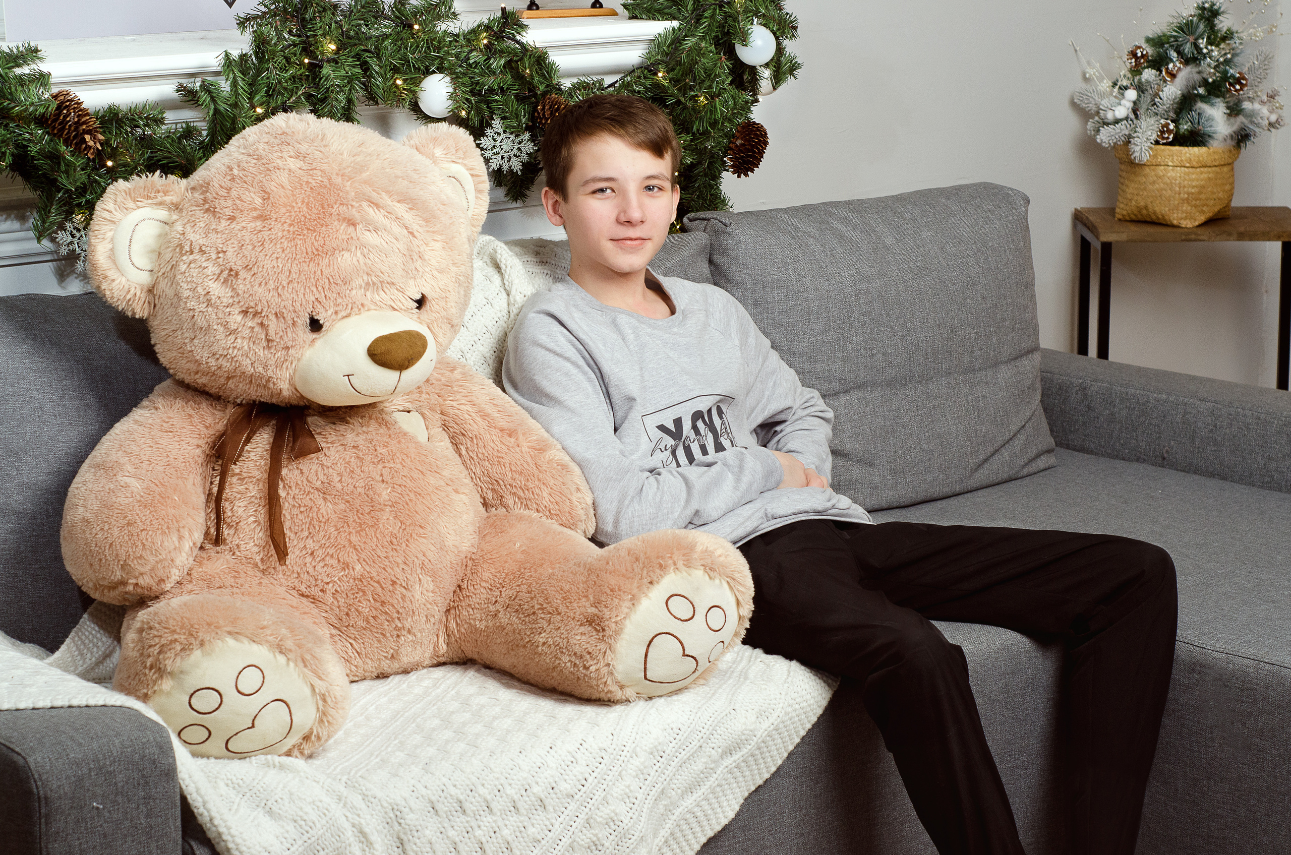 Большой медведь игрушка рядом с мальчиком , на диване.