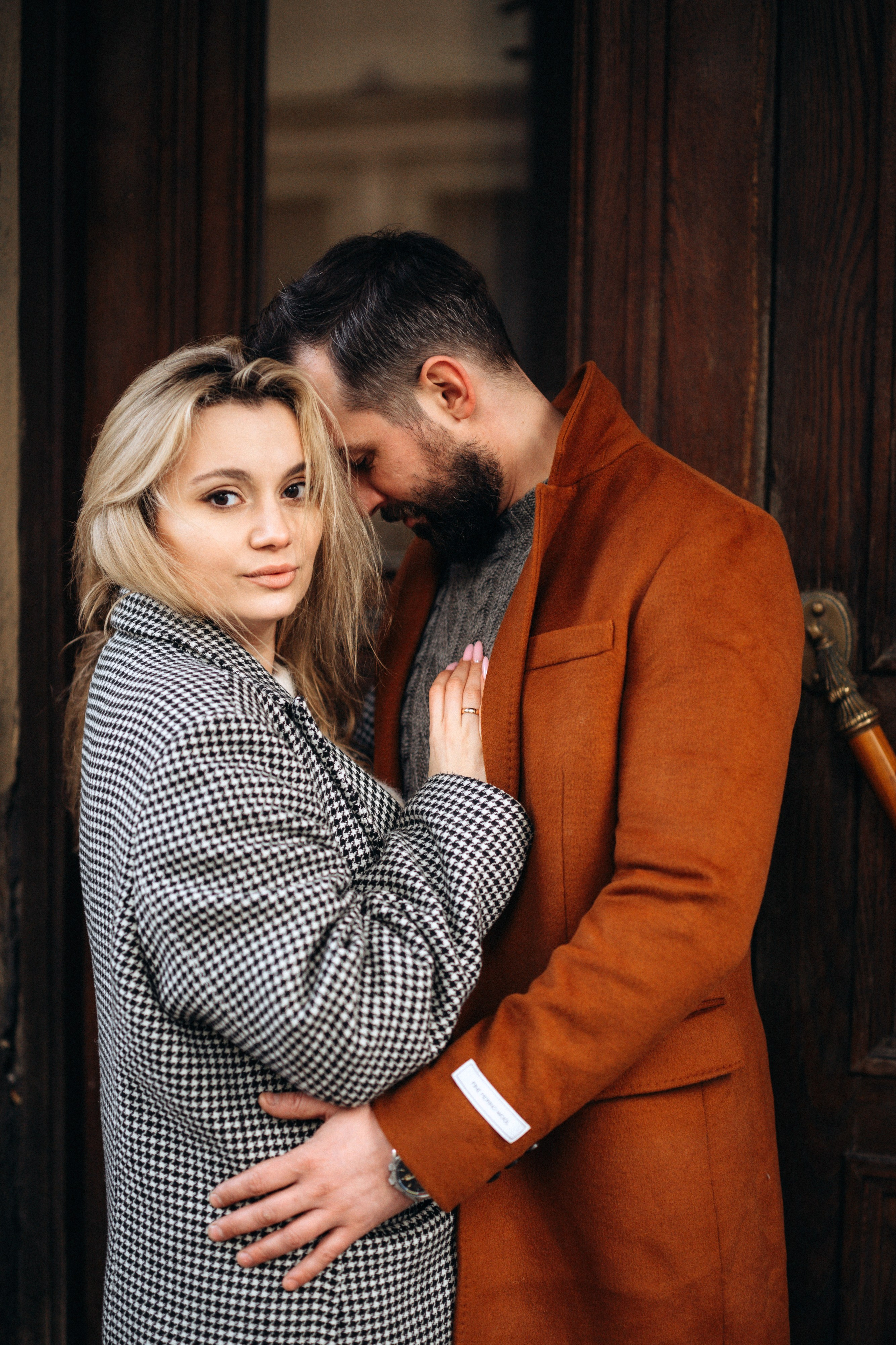 Лавстори Love Story в Санкт-Петербурге с атмосферой города. Пара в коричневых пальто позирует рядом с дверью коричневого цвета.