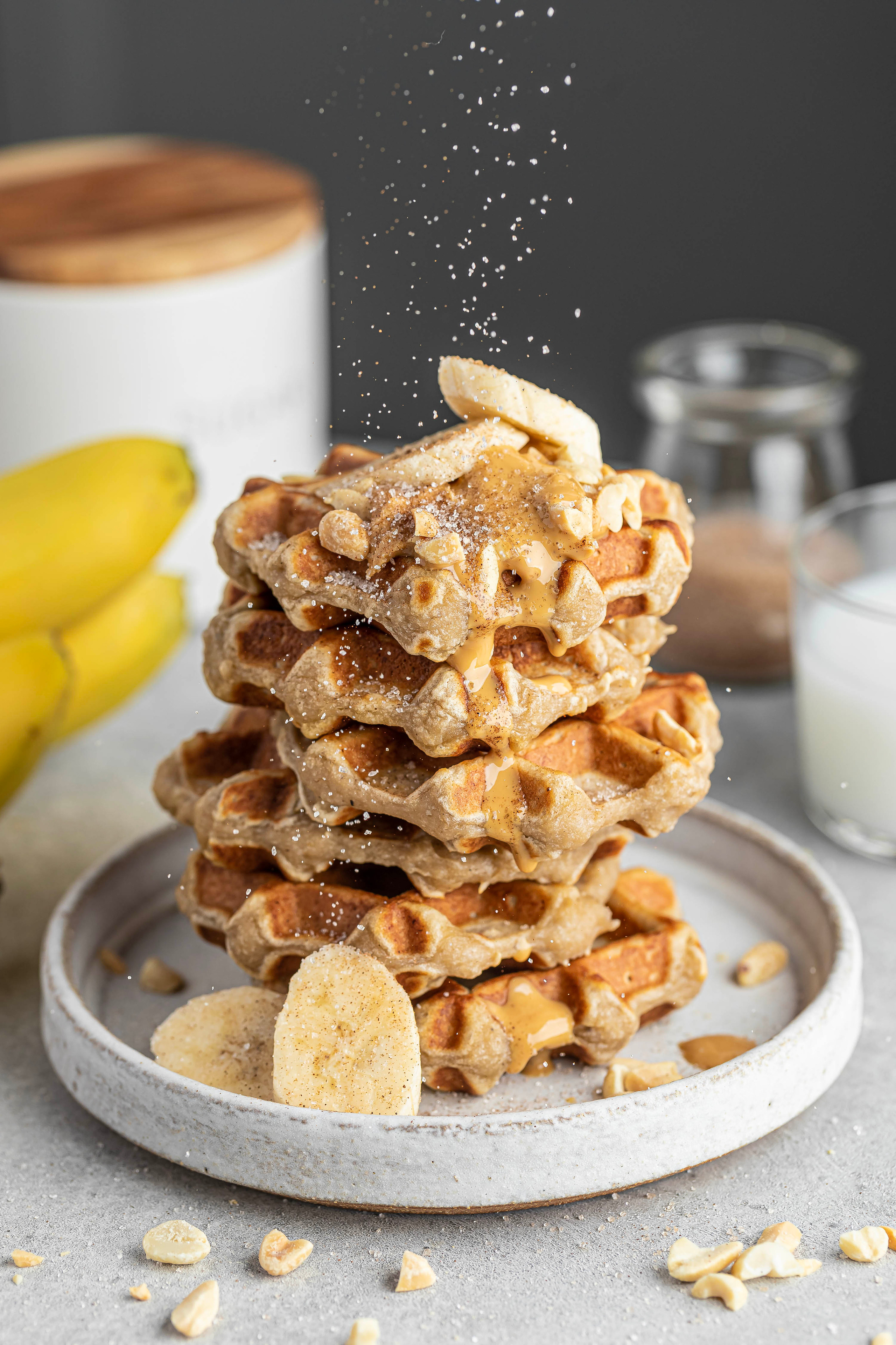 Домашние банановые вафли, украшенные арахисовой пастой свежим бананом, лежат на светлой керамической тарелке, 