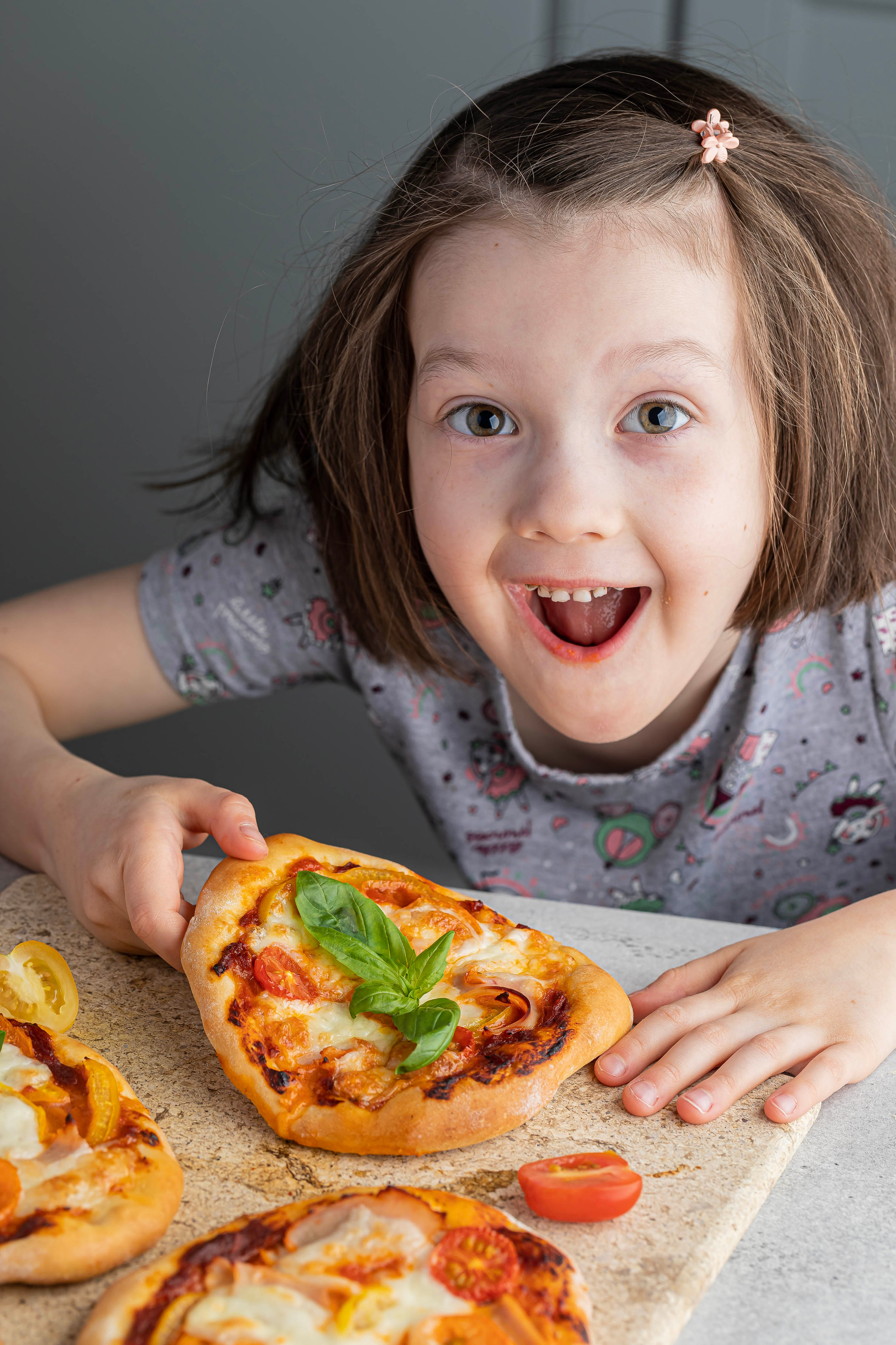 Девочка шести лет смеется и держит в раках мини пиццу, которую она сама готовила